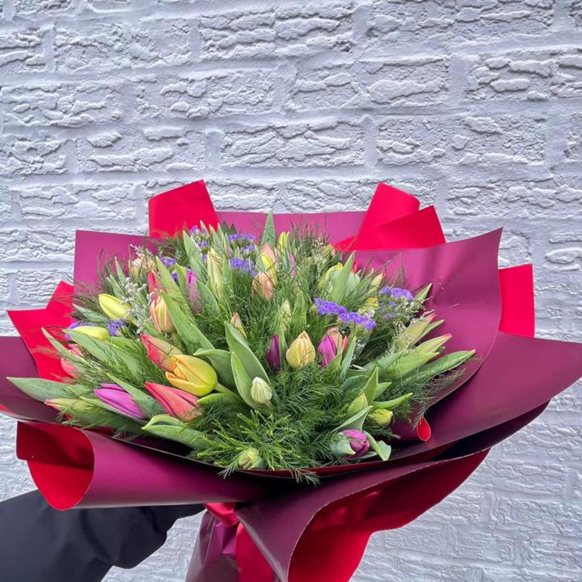 Handheld bouquet of multicolored tulips wrapped in burgundy paper