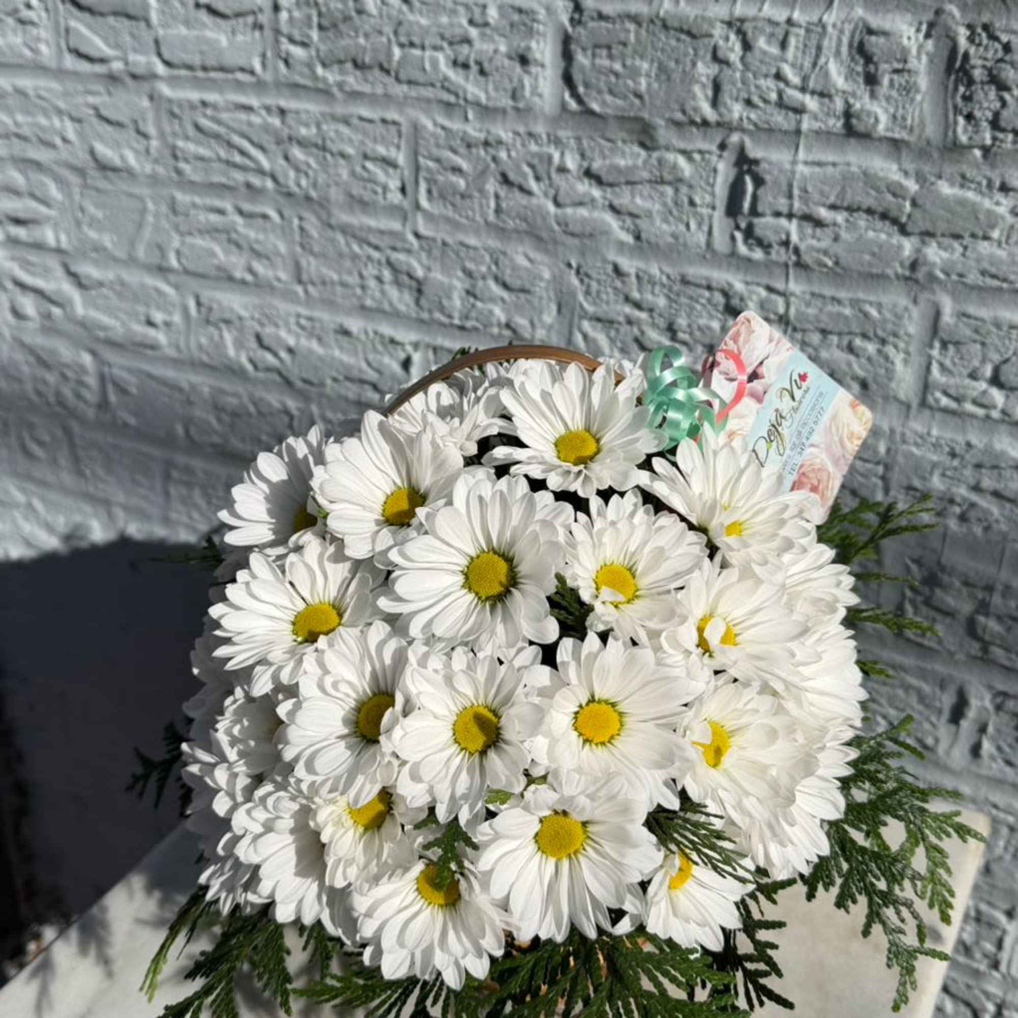 White daisy bouquet with yellow centers and greenery in a basket