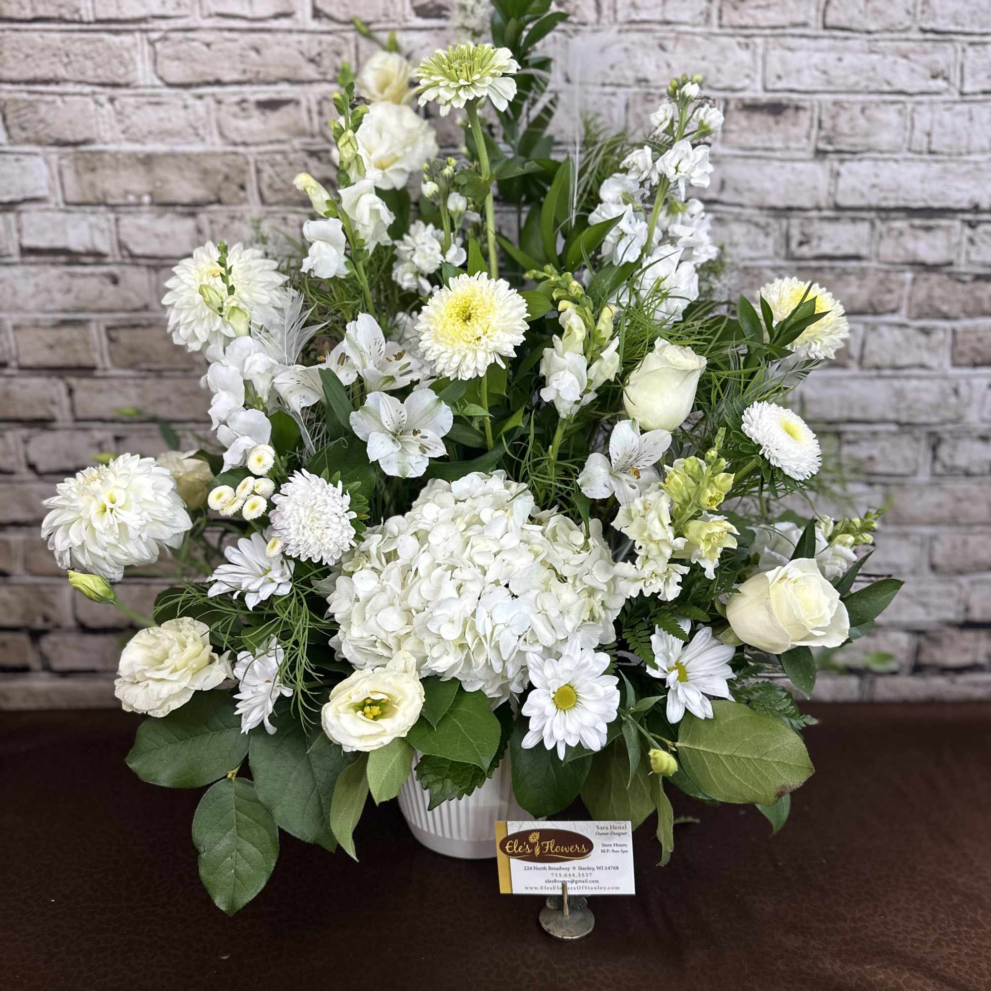 Tall white floral arrangement with hydrangeas, roses, daisies, and mums in a white ceramic container.