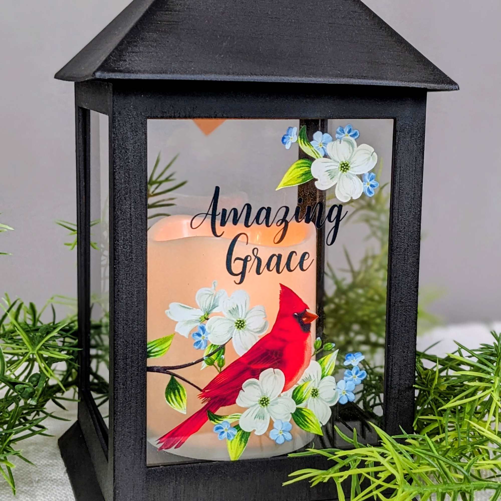 Black lantern candle holder with a lit candle and floral bird design