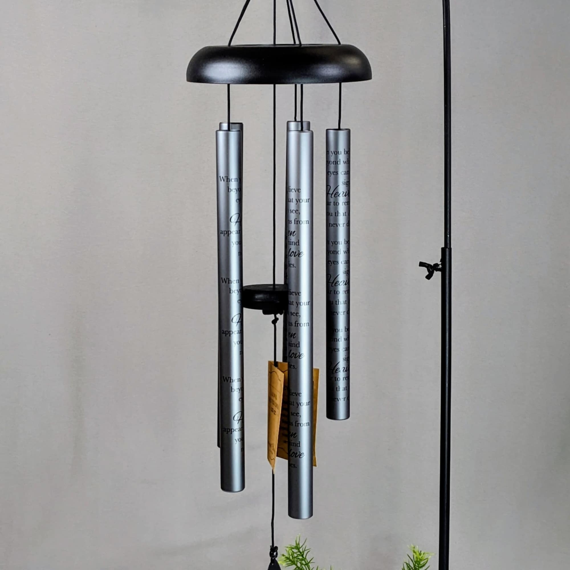 Black metal wind chime stand with silver tubes and green faux foliage