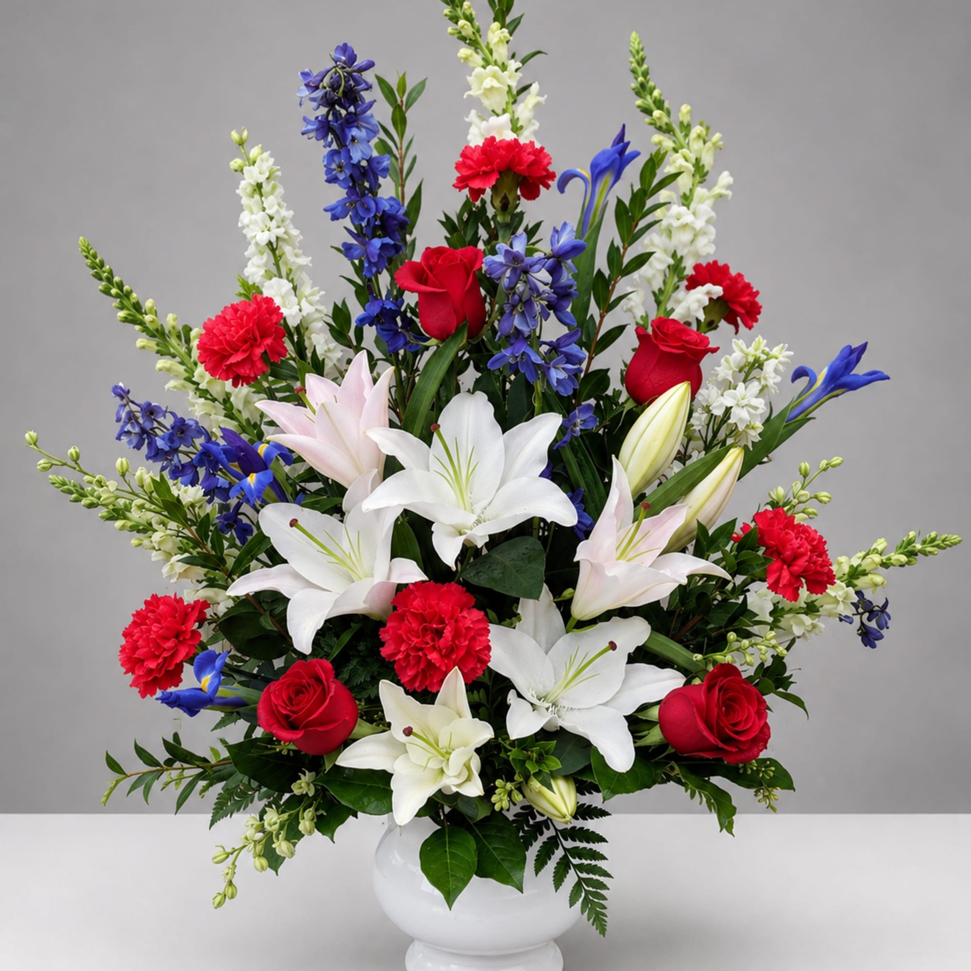 Large mixed bouquet in a white vase with red, white, blue, and pink flowers.