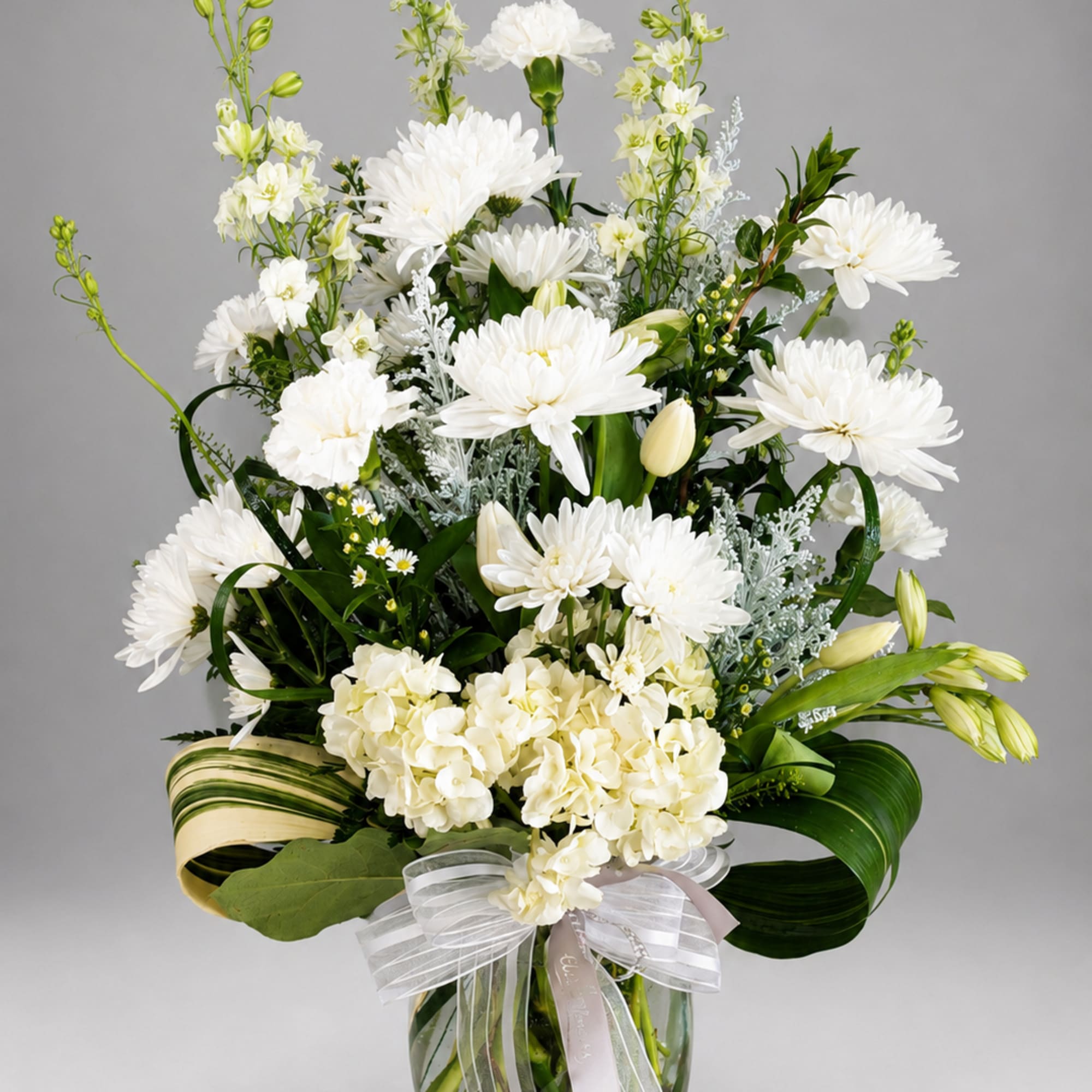 White floral arrangement in a glass vase with a ribbon bow
