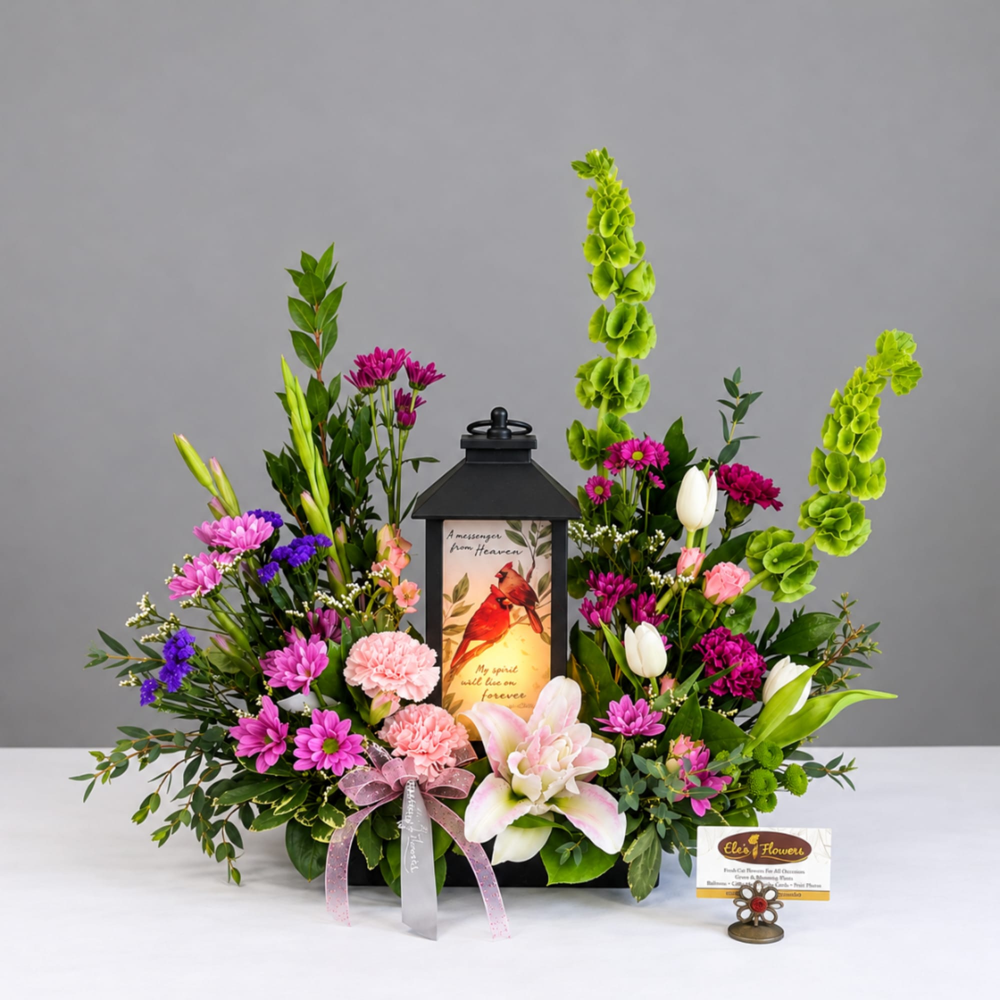 Floral sympathy arrangement around a black lantern with pink and purple blooms