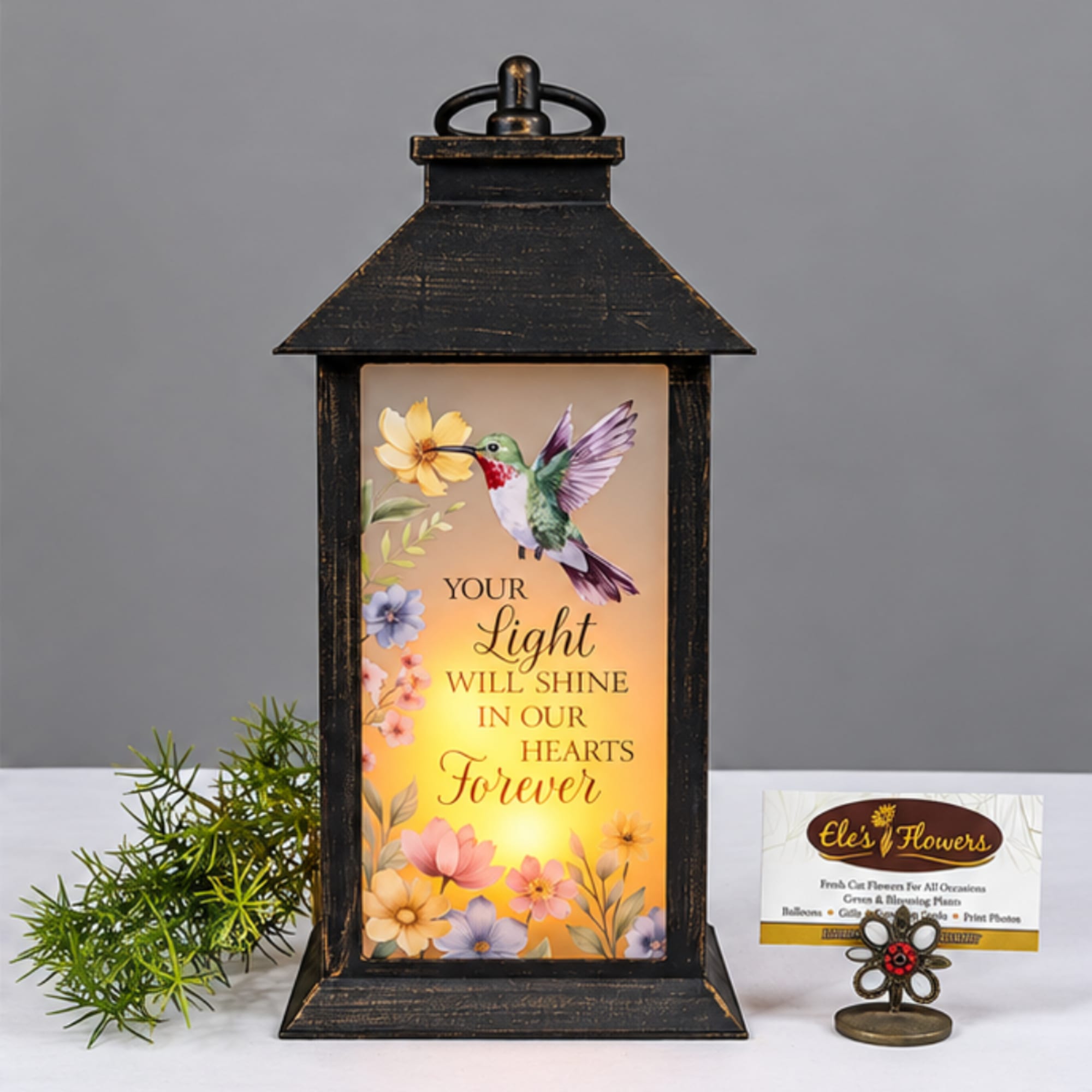 Black lantern with a hummingbird memorial sign and small floral accents