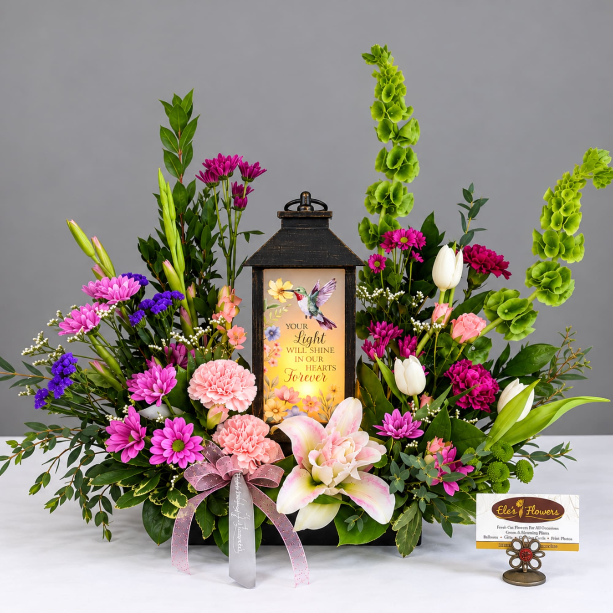 Pink and white floral arrangement around a memorial lantern with a ribbon bow.
