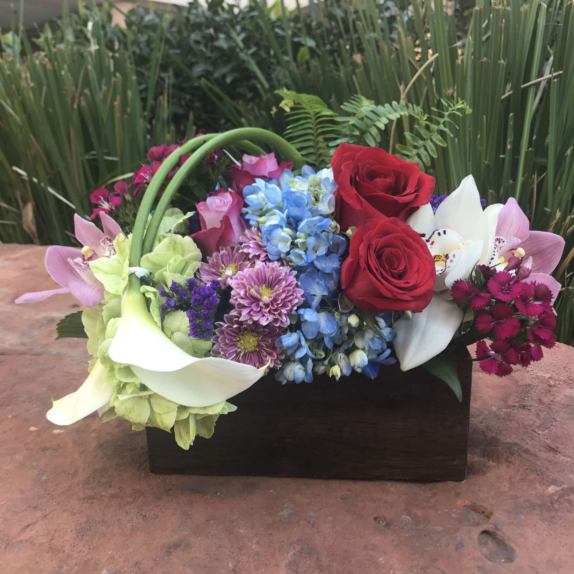 Mixed bouquet with red roses, blue hydrangea, white calla lilies, and pink orchids in a black box