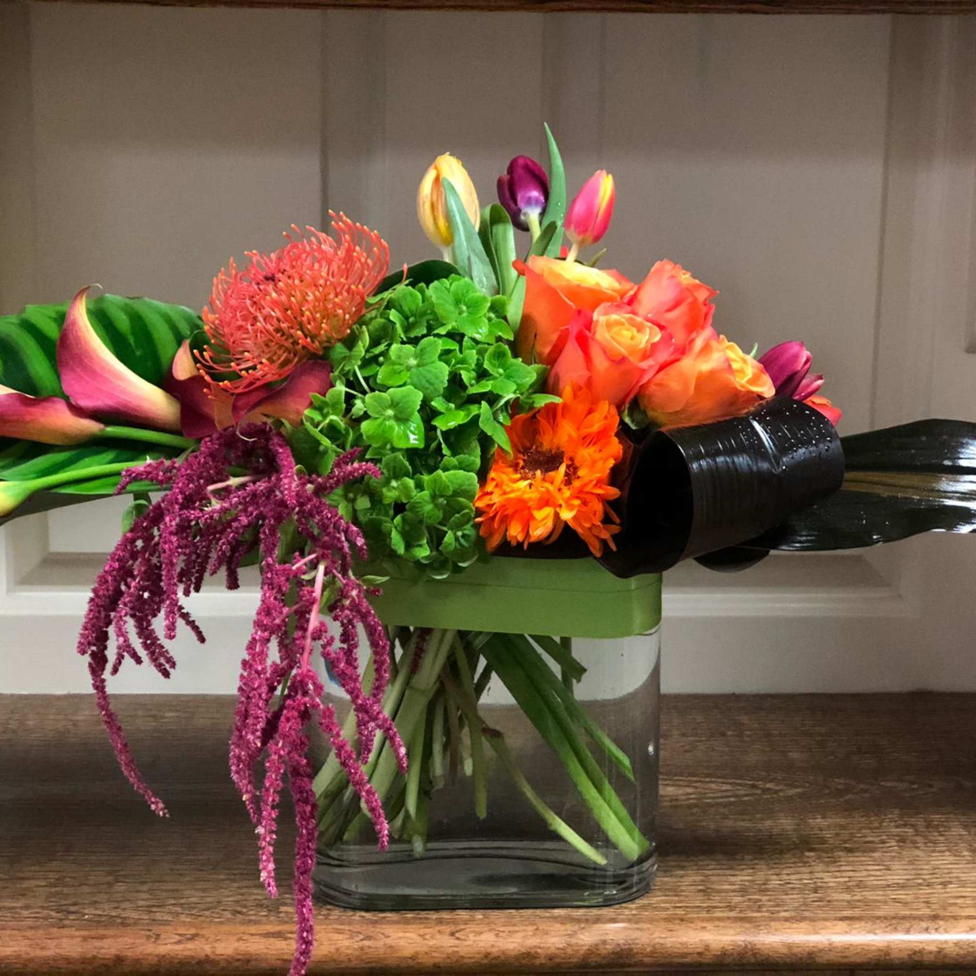 Colorful mixed bouquet in a clear square vase with calla lilies and roses
