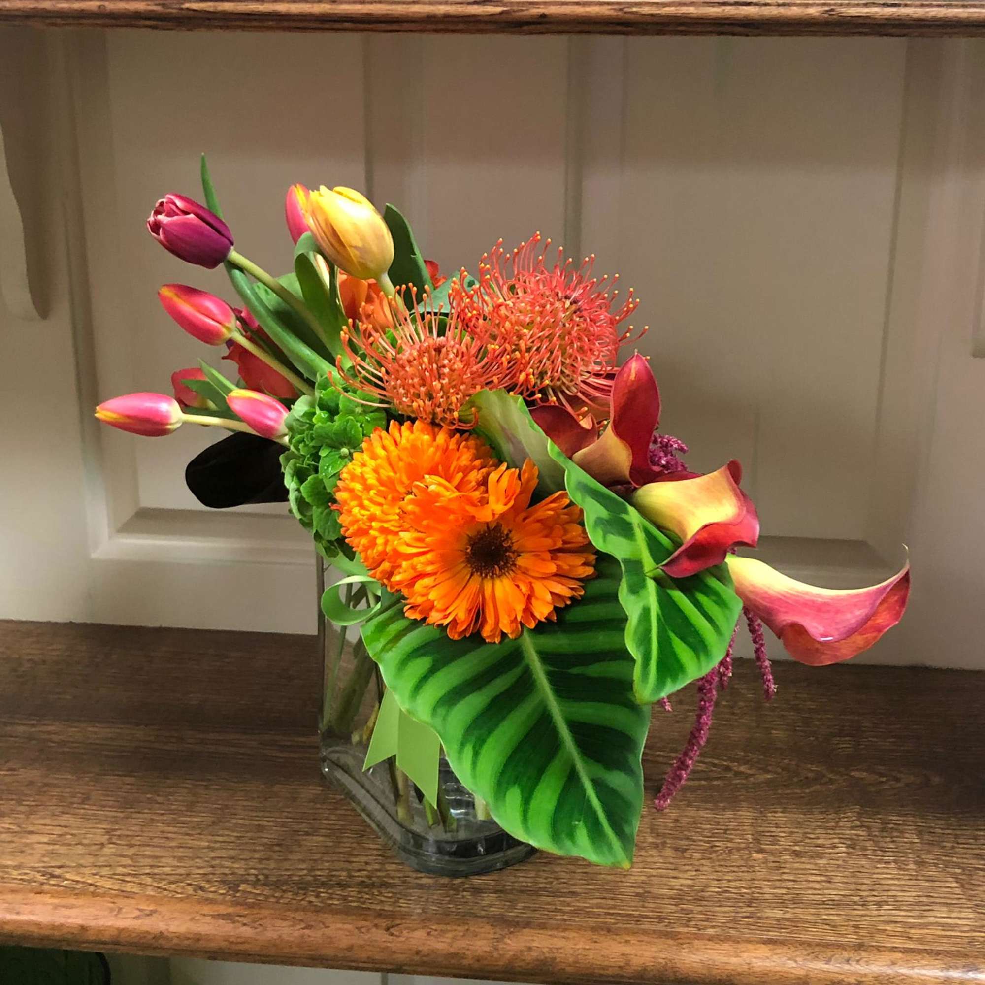 Colorful bouquet with tulips, orange gerbera daisy, calla lilies, and a glass vase