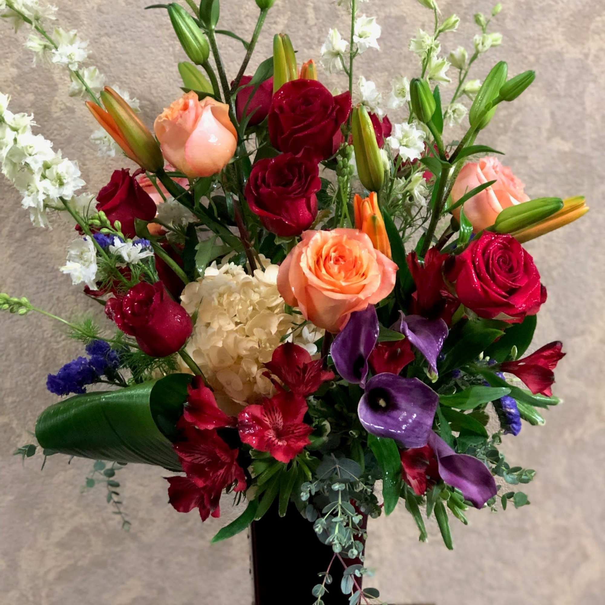 Mixed bouquet of roses, lilies, and purple calla lilies in a tall black vase