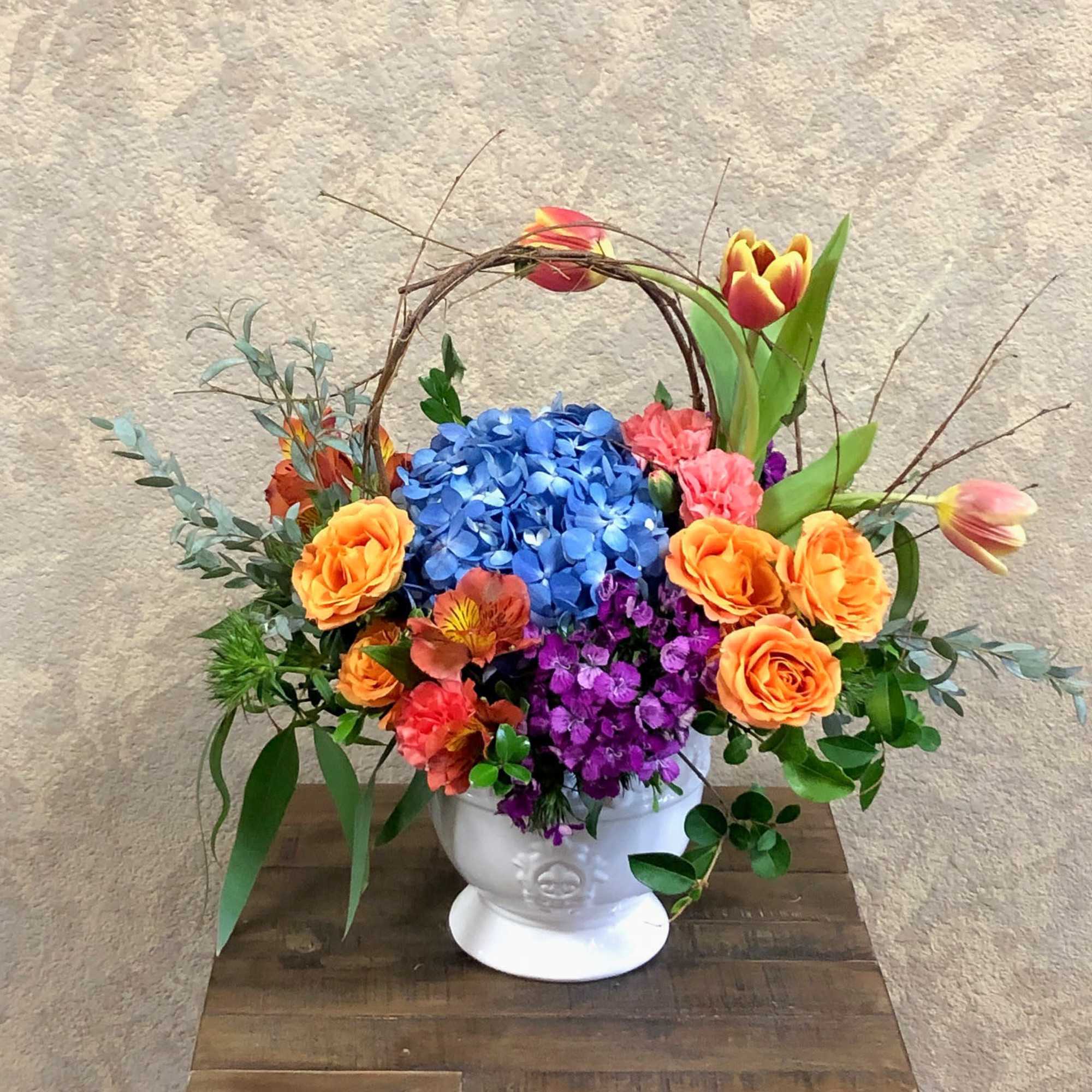 Colorful flower arrangement in a white pedestal vase with a twig handle