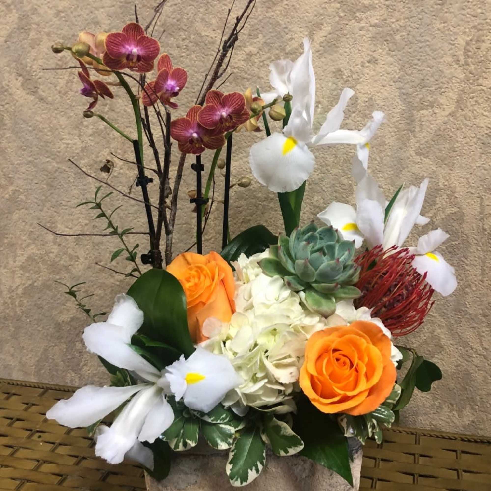 Mixed floral arrangement with orange roses, white orchids, and a succulent in a stone container