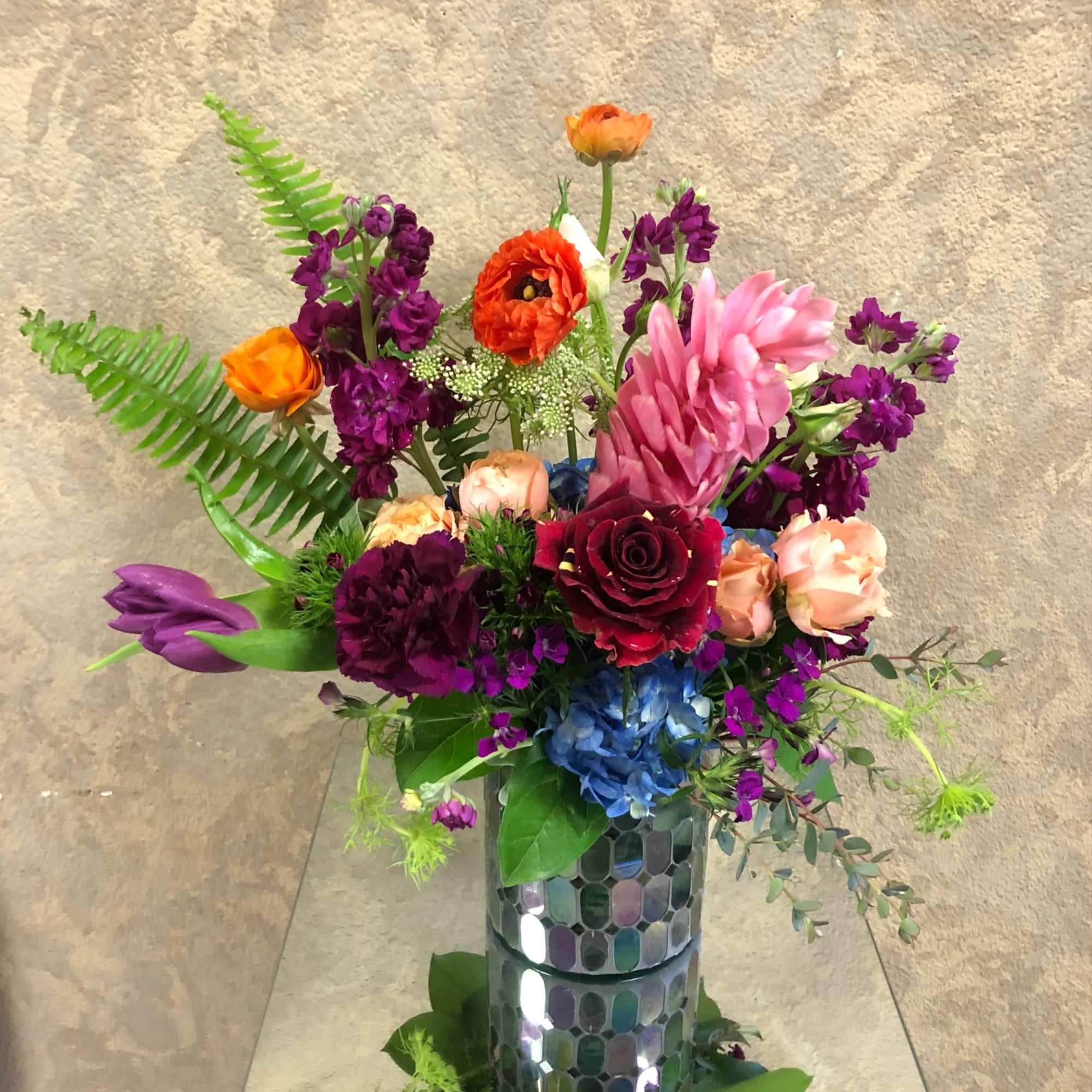 Colorful mixed bouquet in a mirrored vase with pink, purple, orange, and blue blooms