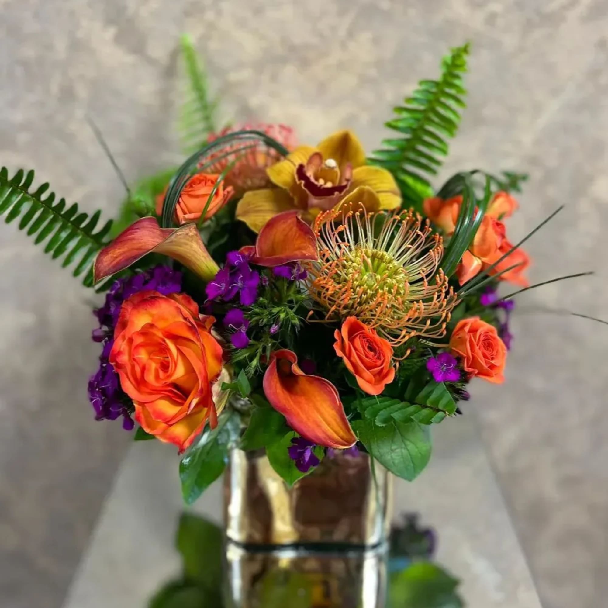 Orange roses and tropical blooms in a glass vase