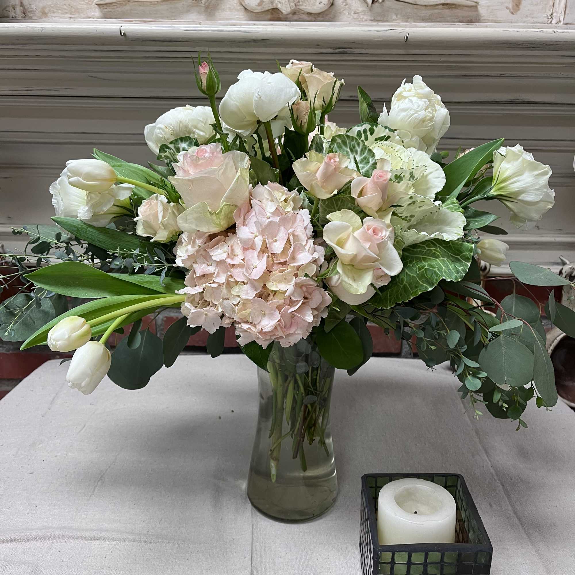 White and blush floral arrangement in a glass vase with a candle nearby
