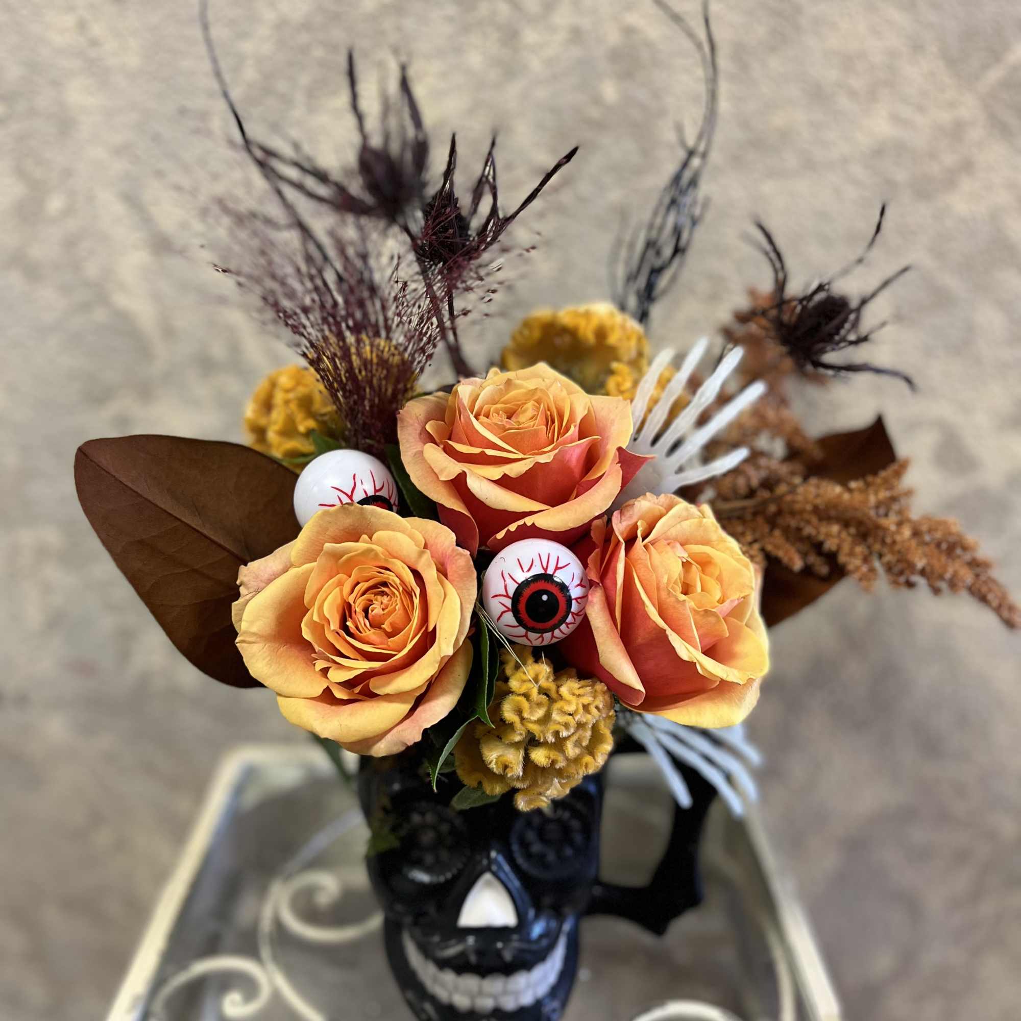 Orange roses arranged in a black skull vase with Halloween decorations