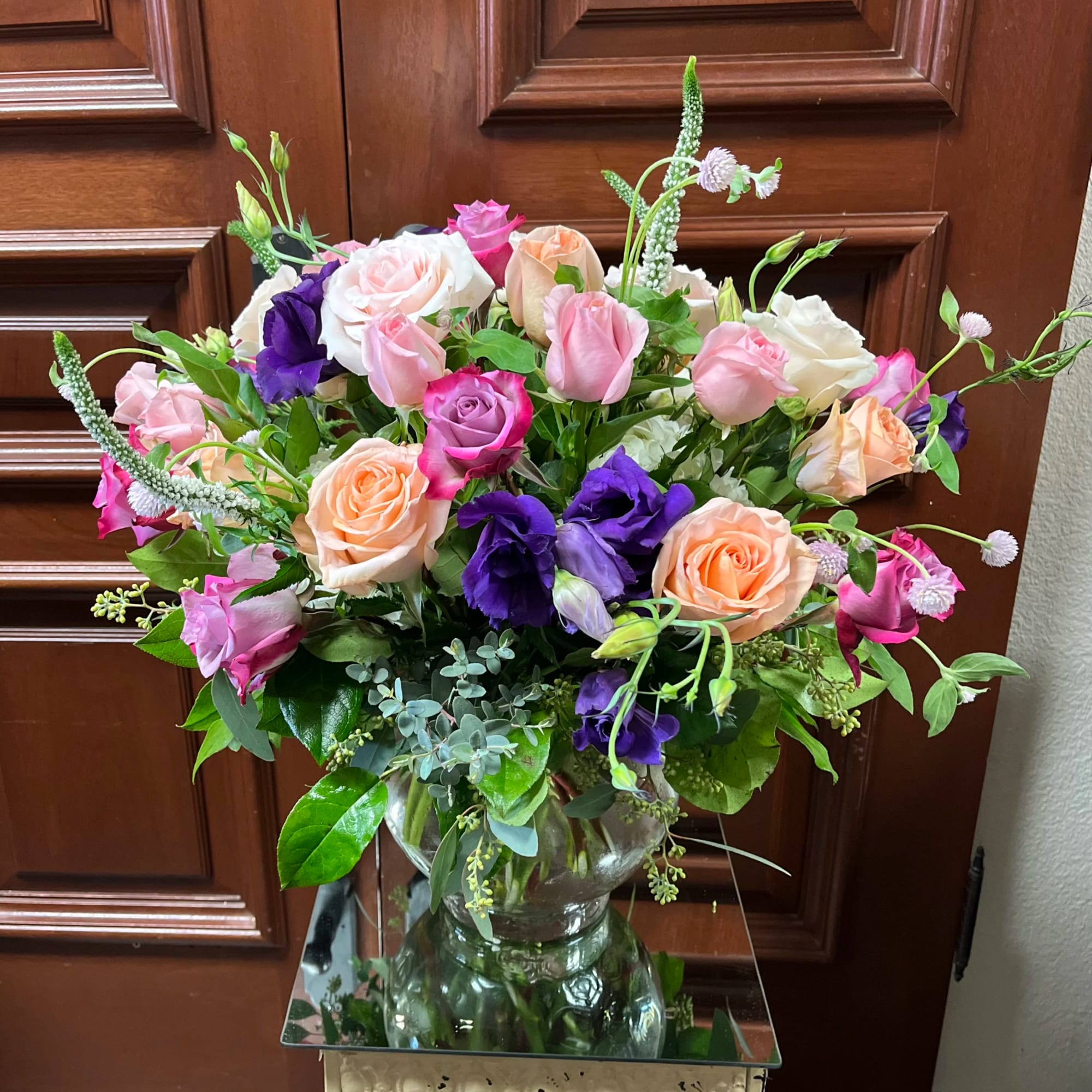 Mixed bouquet of pink, peach, white, and purple roses in a glass vase