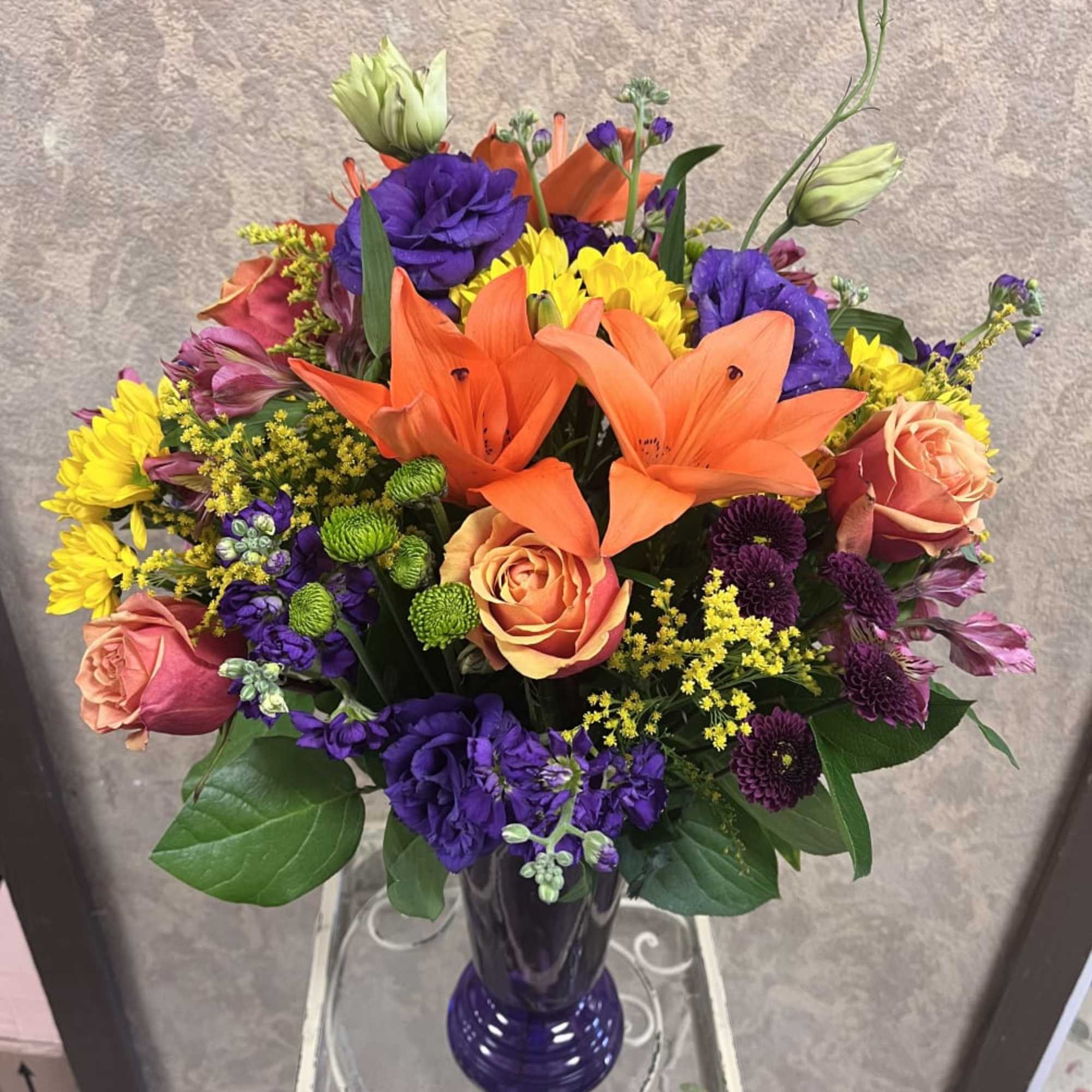 Colorful bouquet with orange lilies, roses, and purple blooms in a blue vase