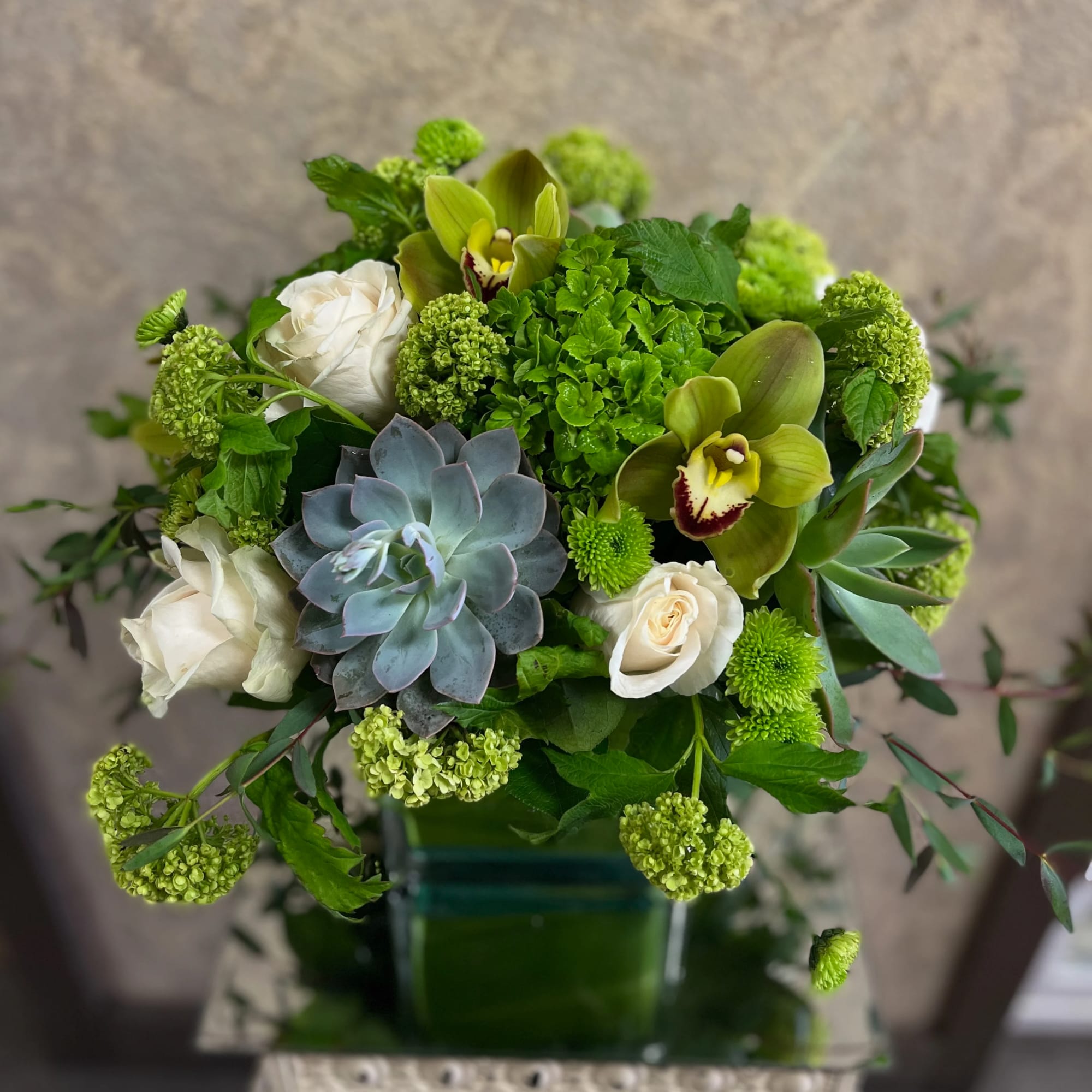 Green and white bouquet with orchids, roses, and a succulent in a glass vase