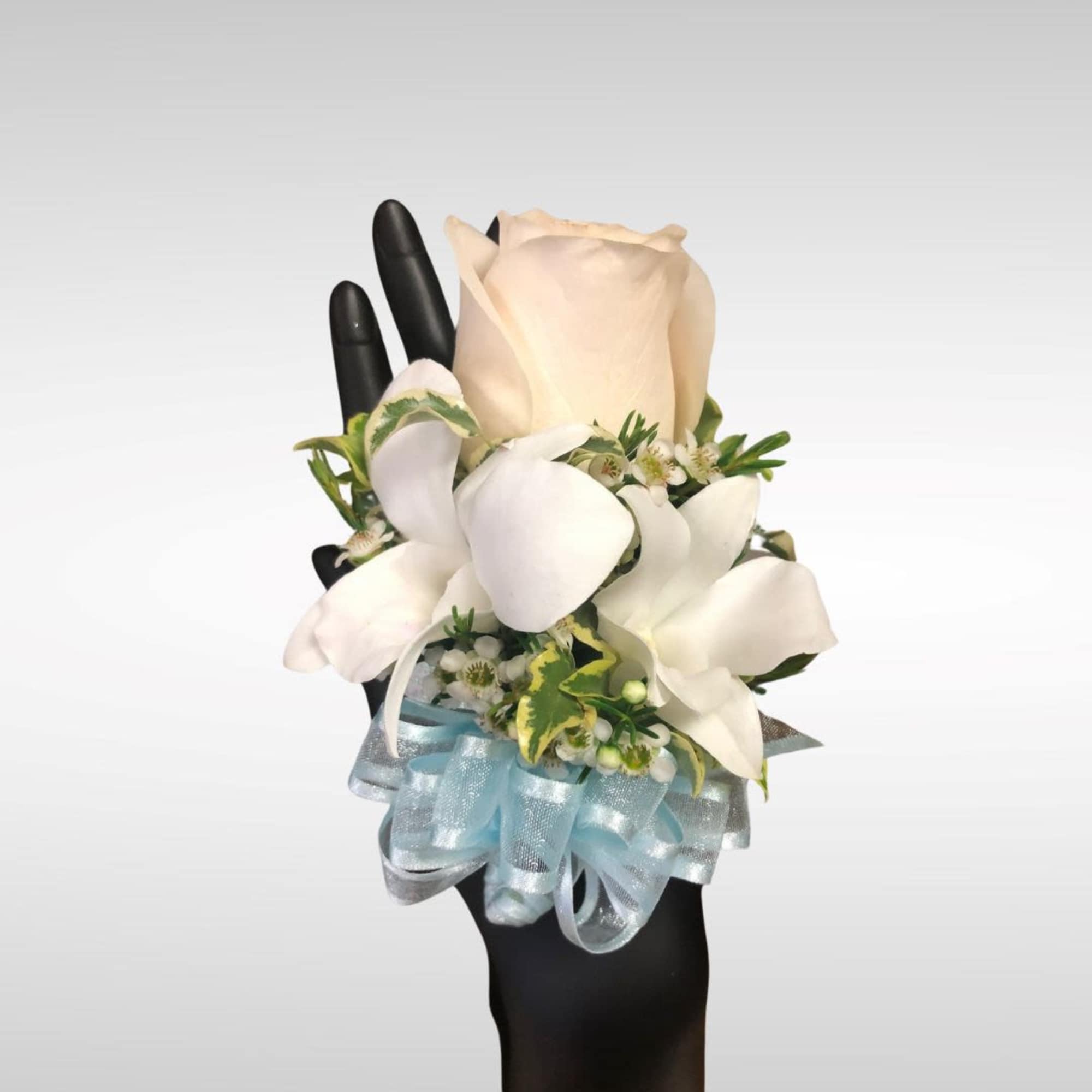 Wrist corsage with cream rose, white blooms, and light blue ribbon on a black mannequin hand
