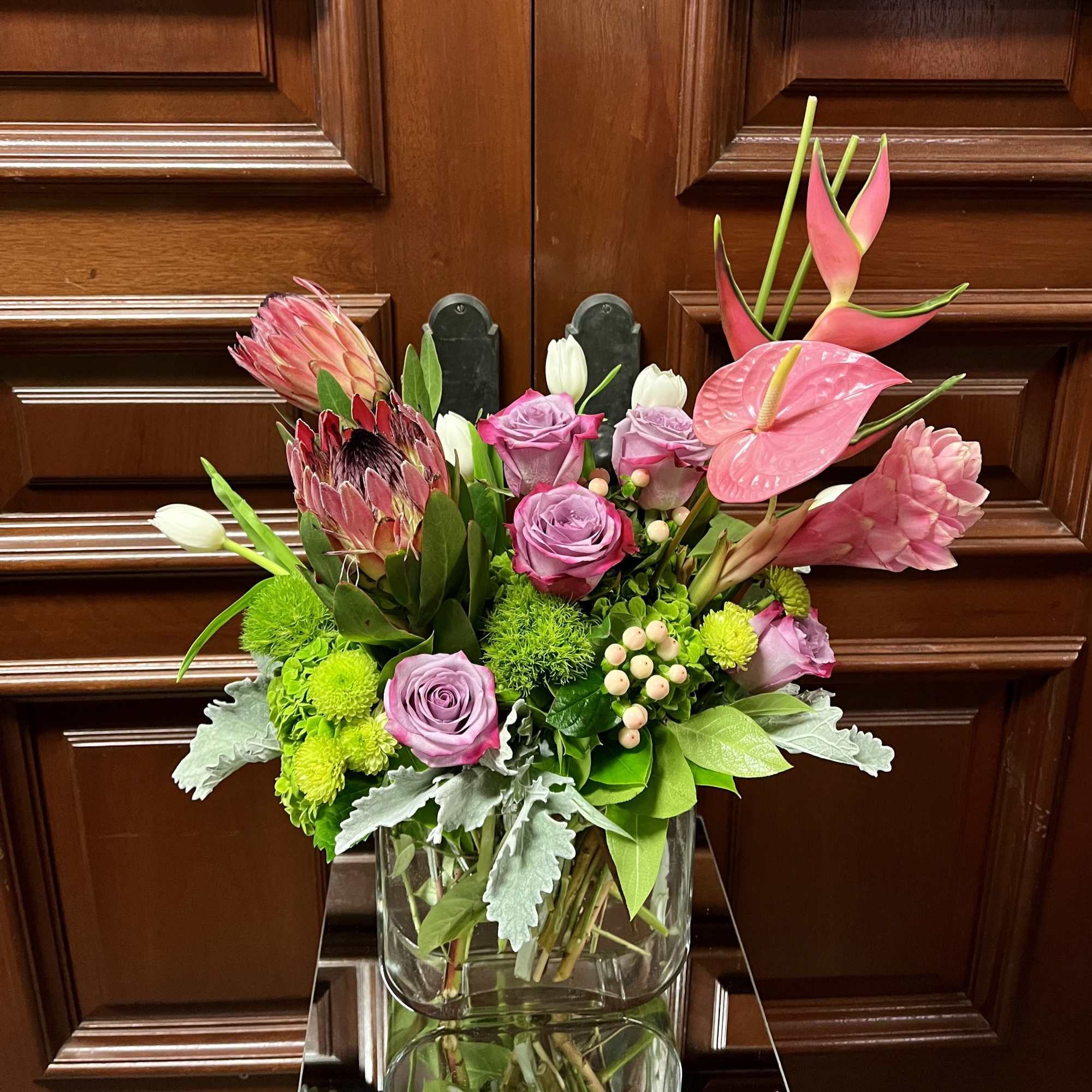 Mixed bouquet of pink roses, protea, and tropical blooms in a glass vase