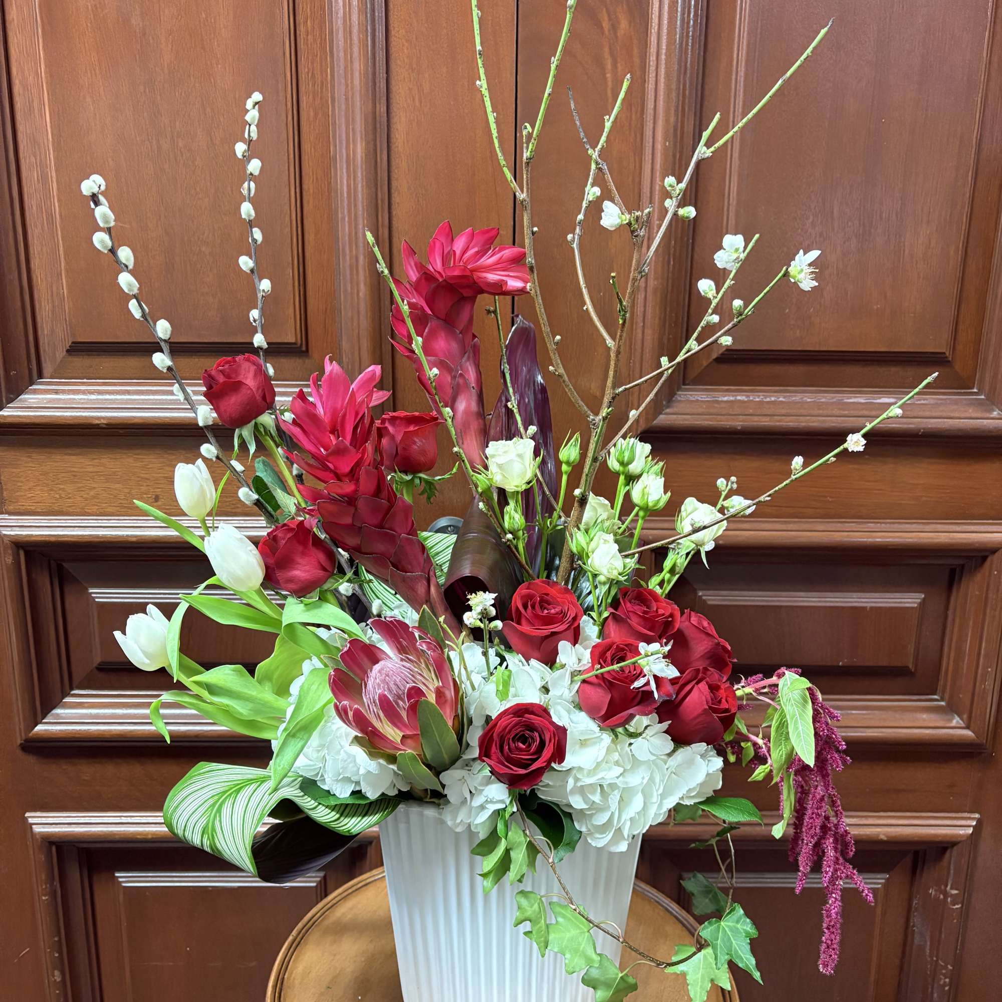Tall floral arrangement with red roses, white blooms, and branching stems in a white vase