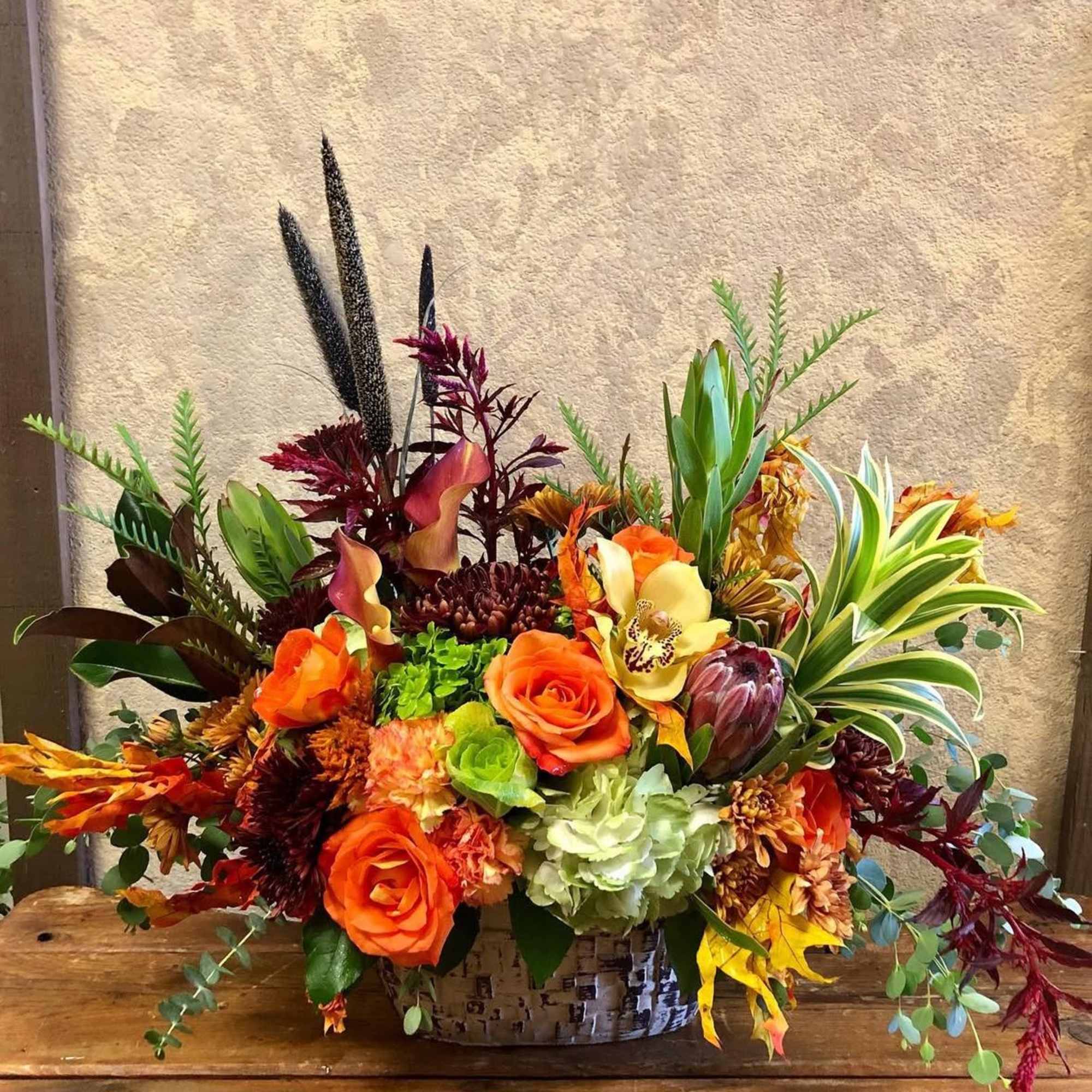 Autumn floral arrangement with orange roses and mixed blooms in a woven basket