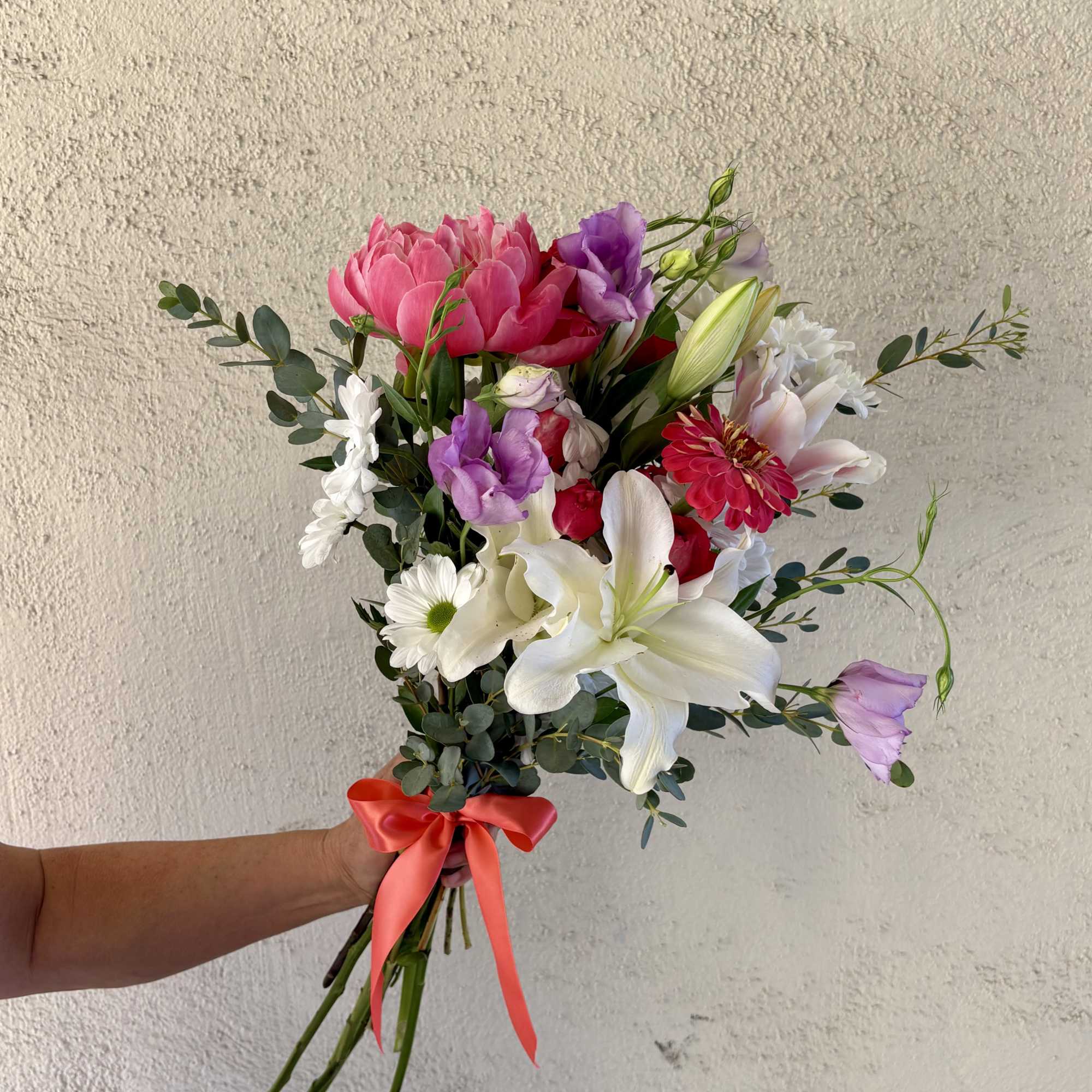 Handheld bouquet of pink, white, and purple flowers tied with a coral ribbon.
