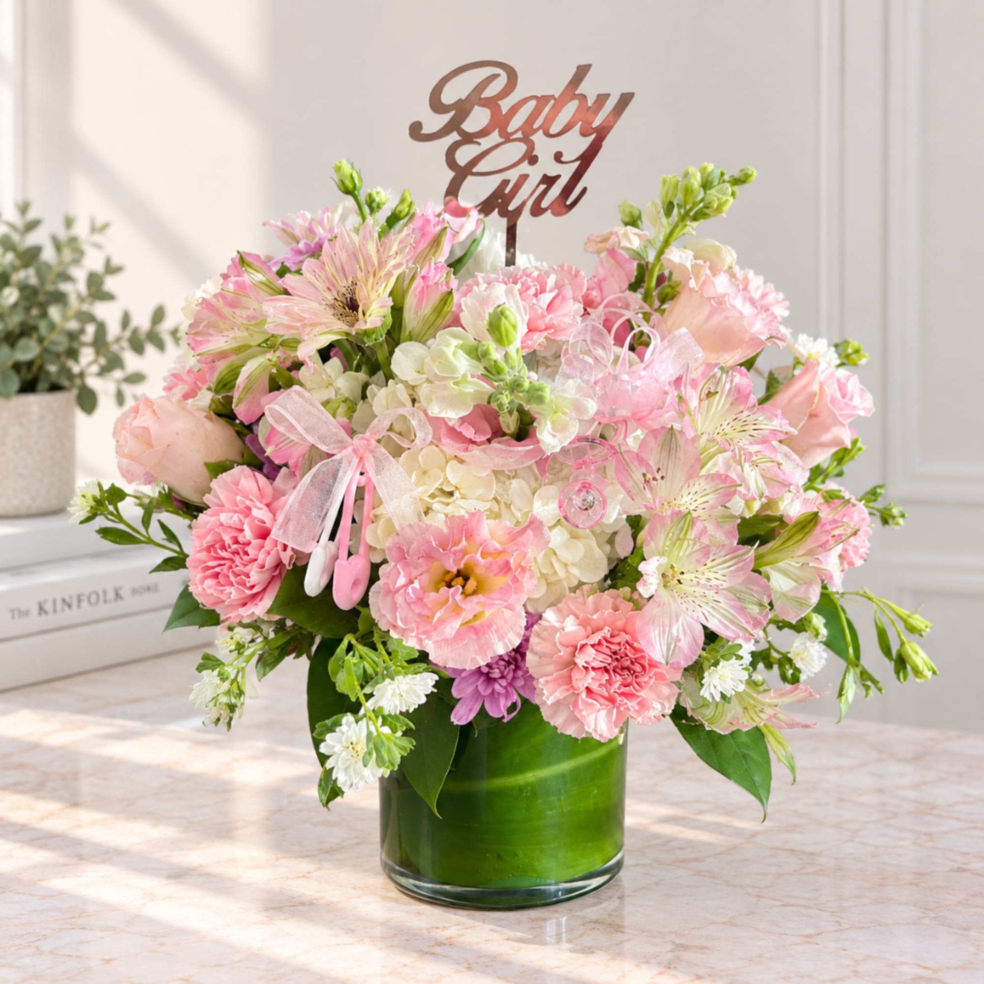Pink and white flower arrangement in a green glass vase with a "Baby Girl" topper