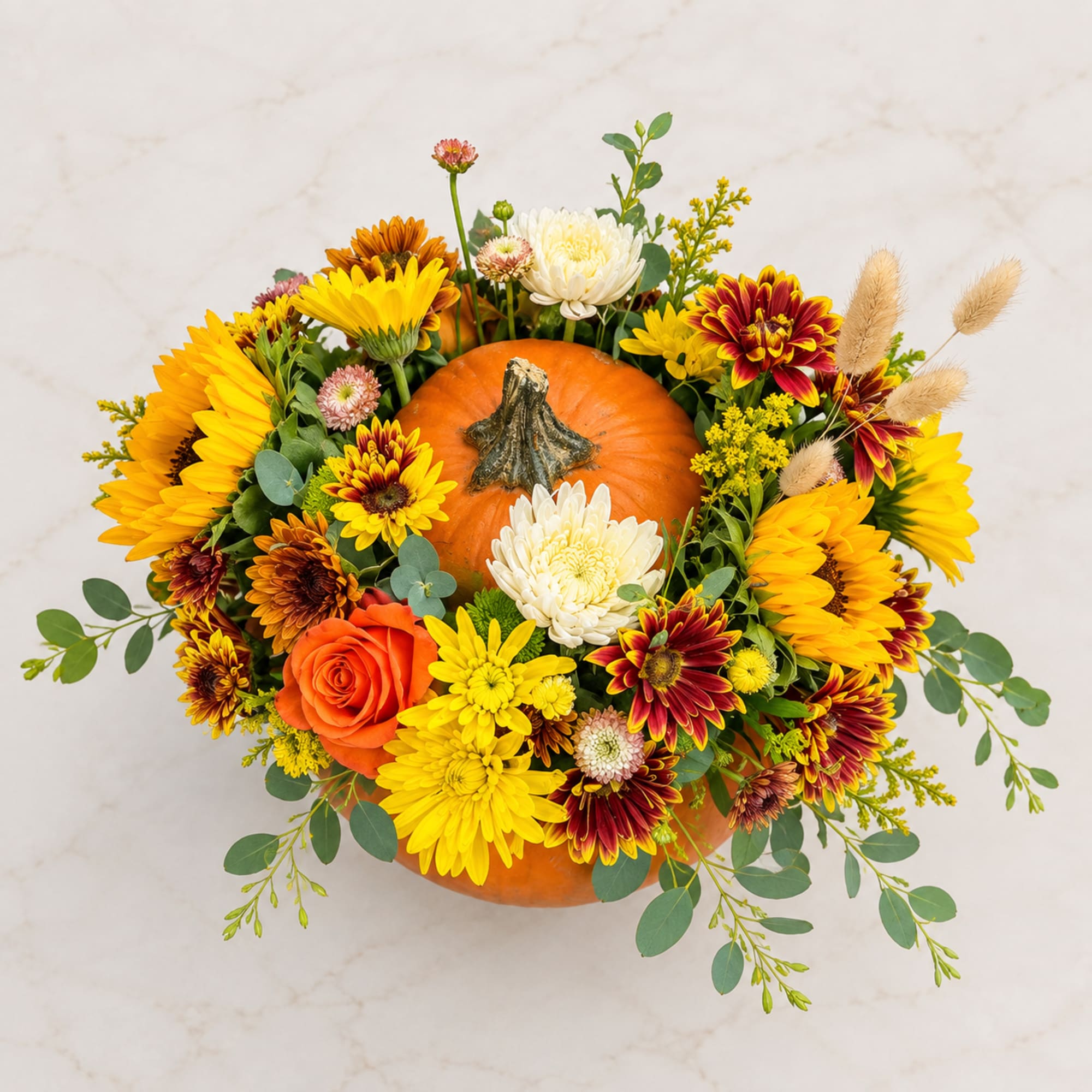 Pumpkin centerpiece with yellow, orange, red, and white flowers
