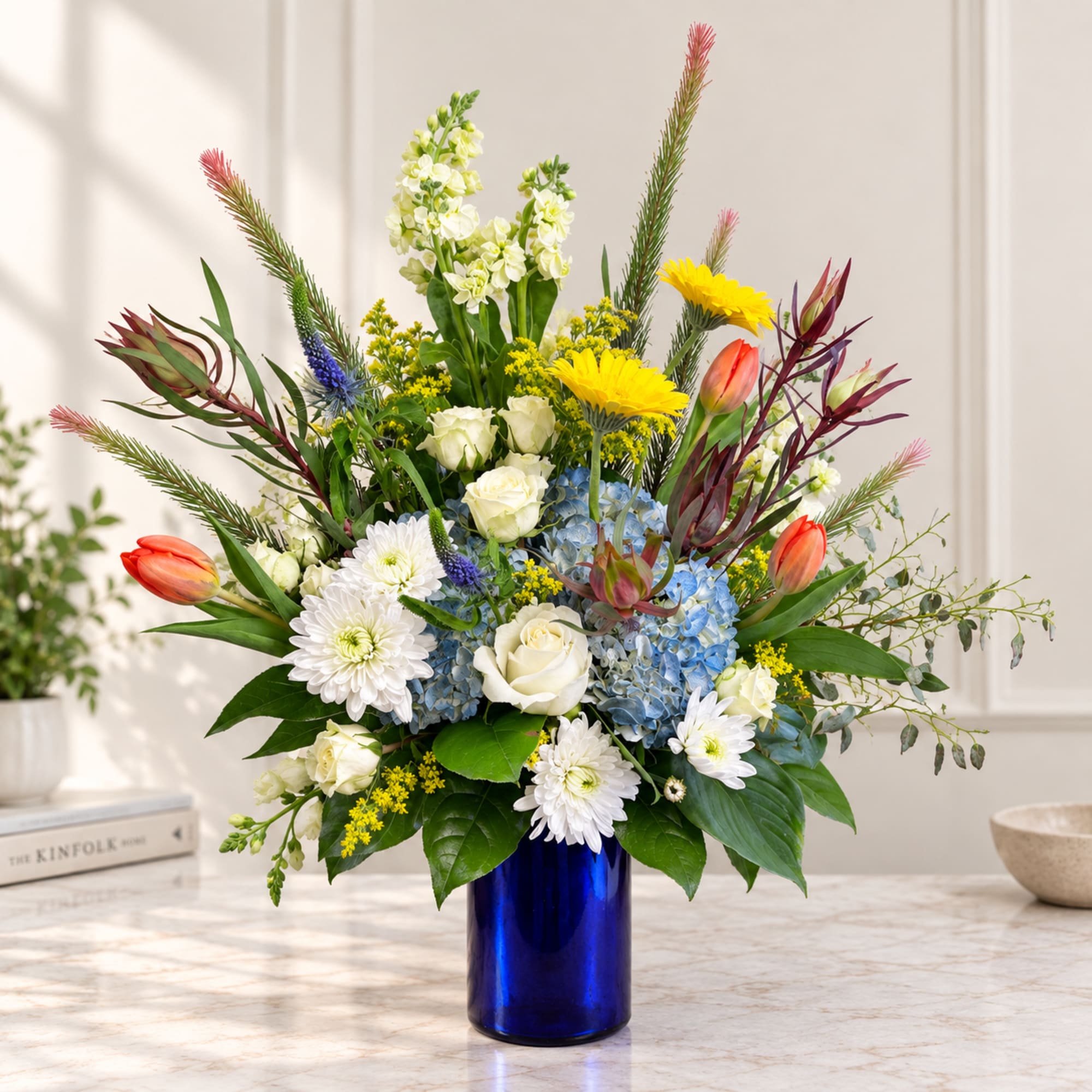 Mixed bouquet in a blue vase with white, yellow, blue, and coral flowers