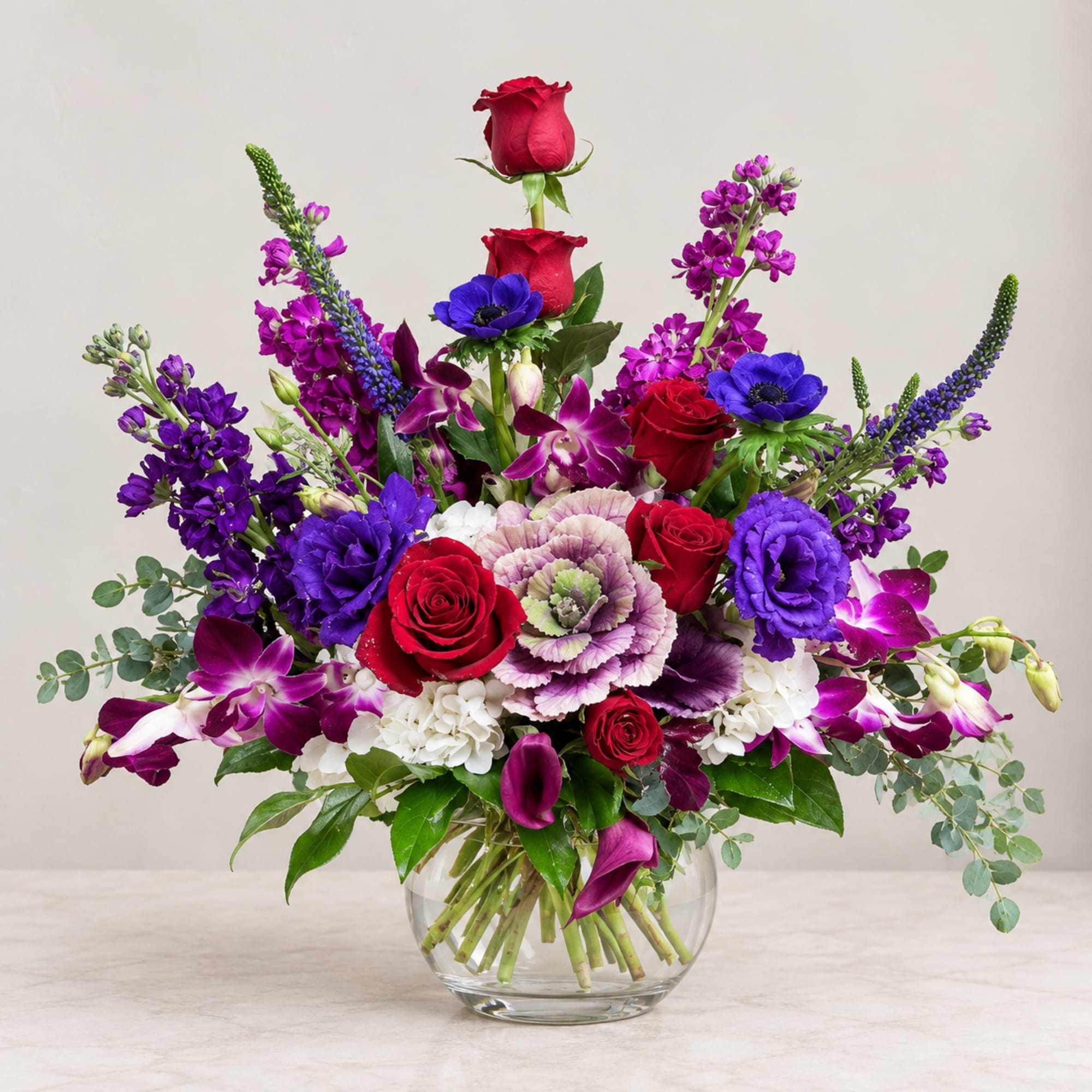 Mixed bouquet of red, purple, and white flowers in a clear glass vase