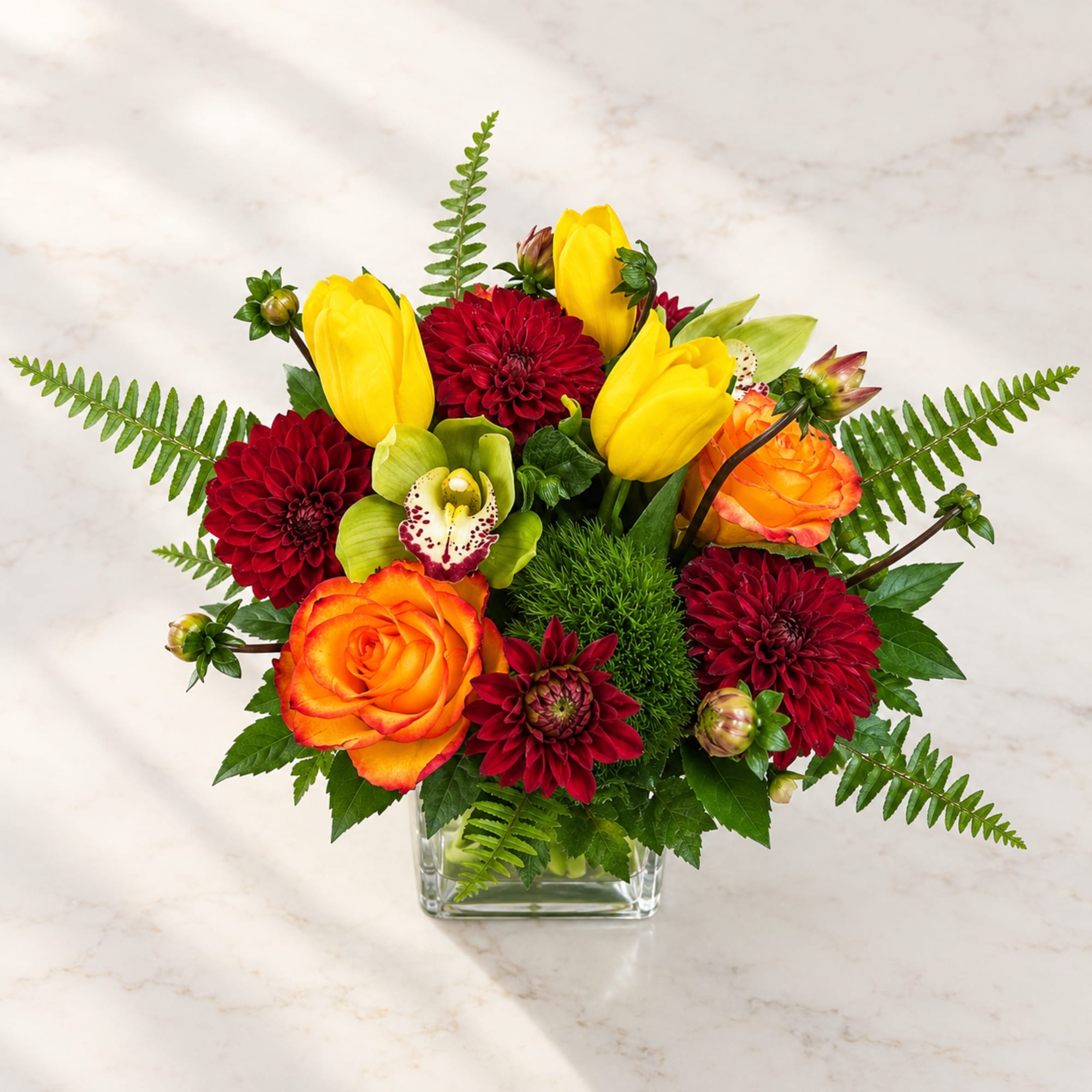 Bright bouquet of yellow tulips, red dahlias, and orange roses in a glass vase