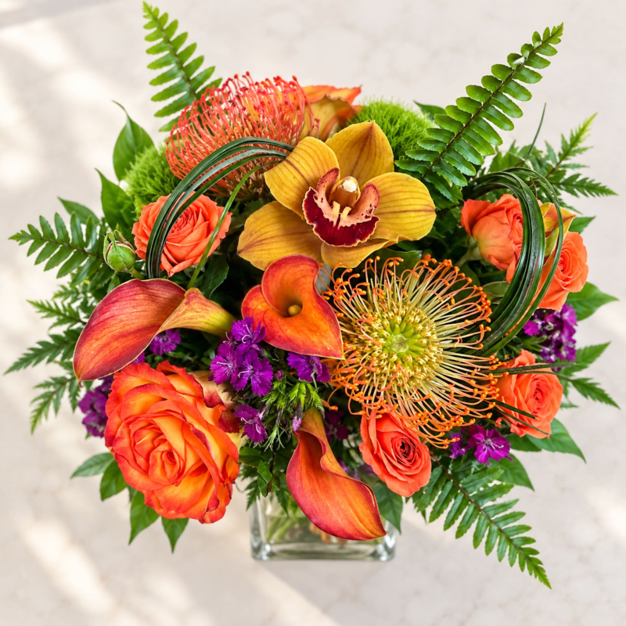 Bright tropical bouquet with orange roses and orchids in a glass vase