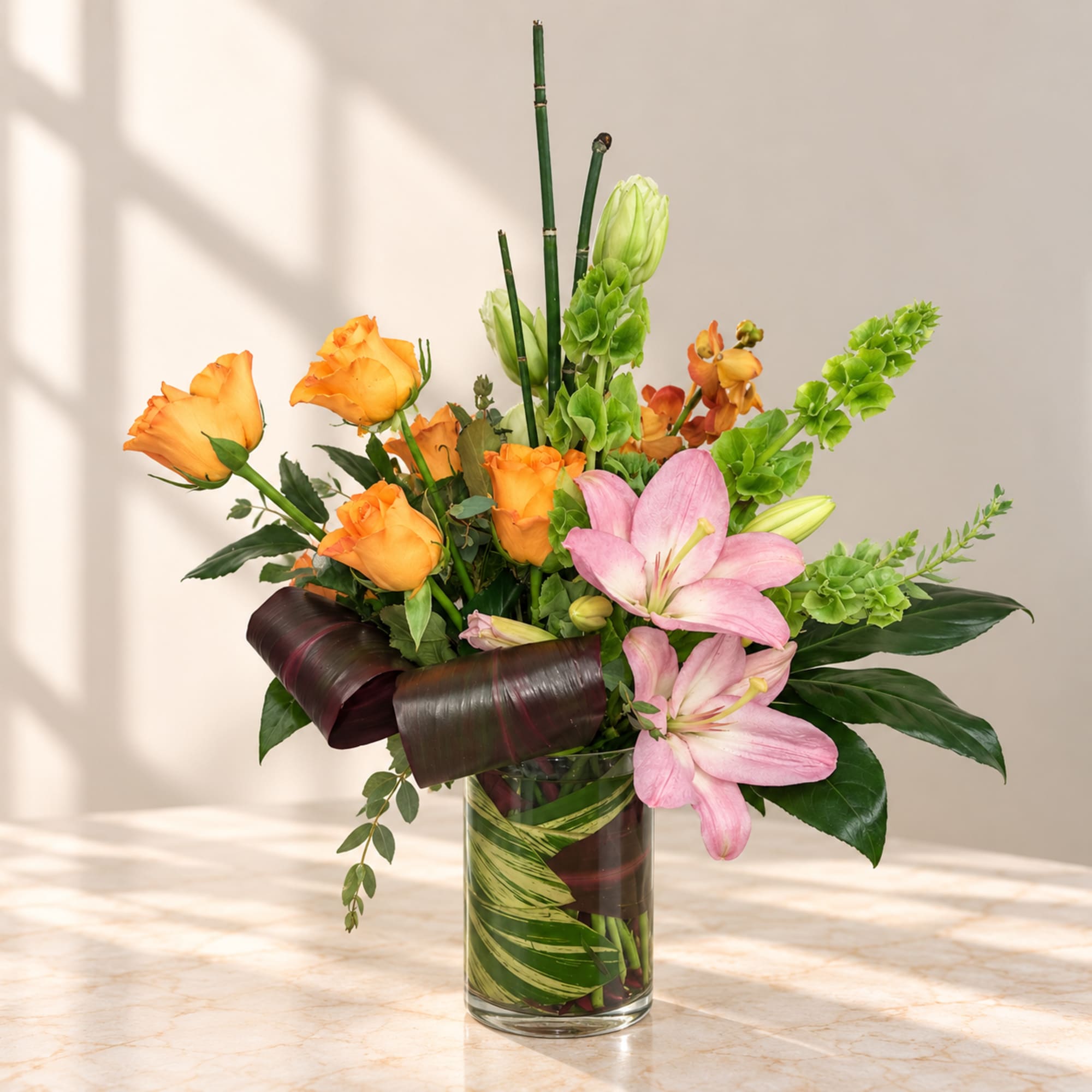 Orange roses and pink lilies in a glass vase with green accents