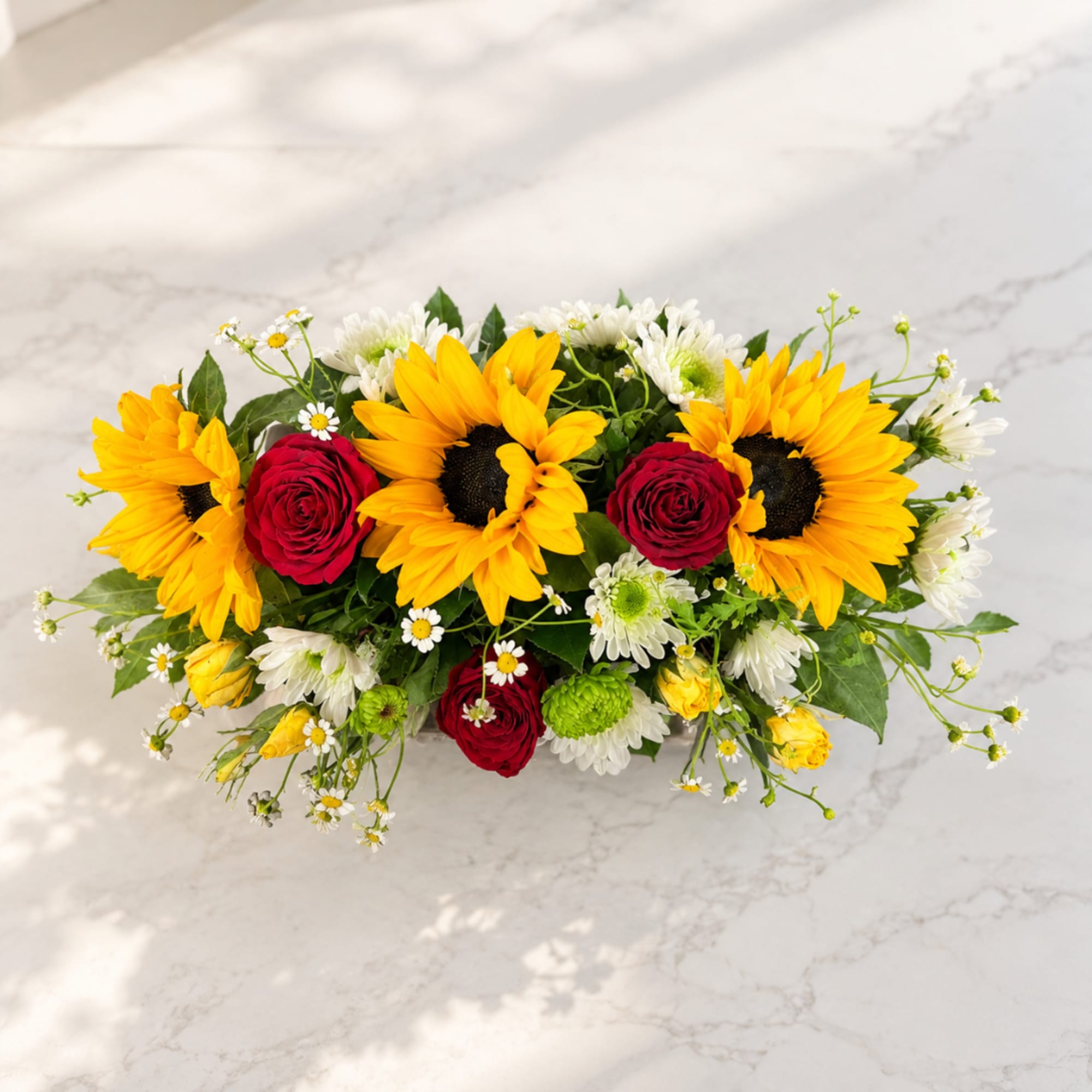 Sunflower and red rose arrangement with white daisies on a low table