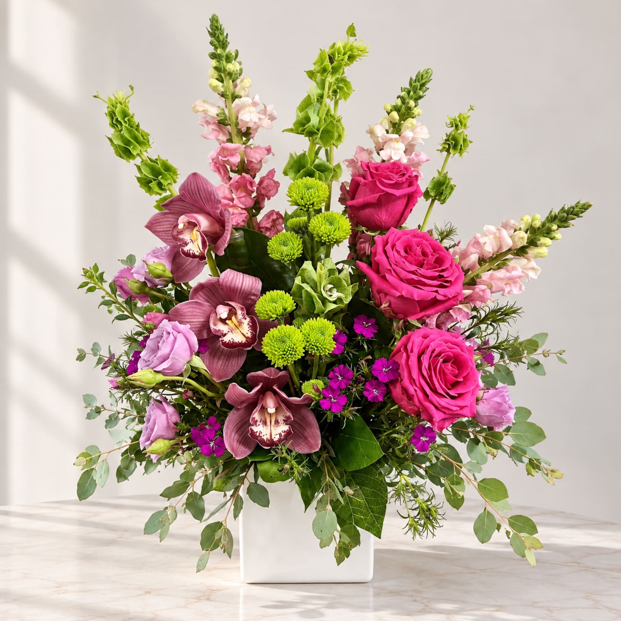Pink roses and orchids in a white square vase with green accents