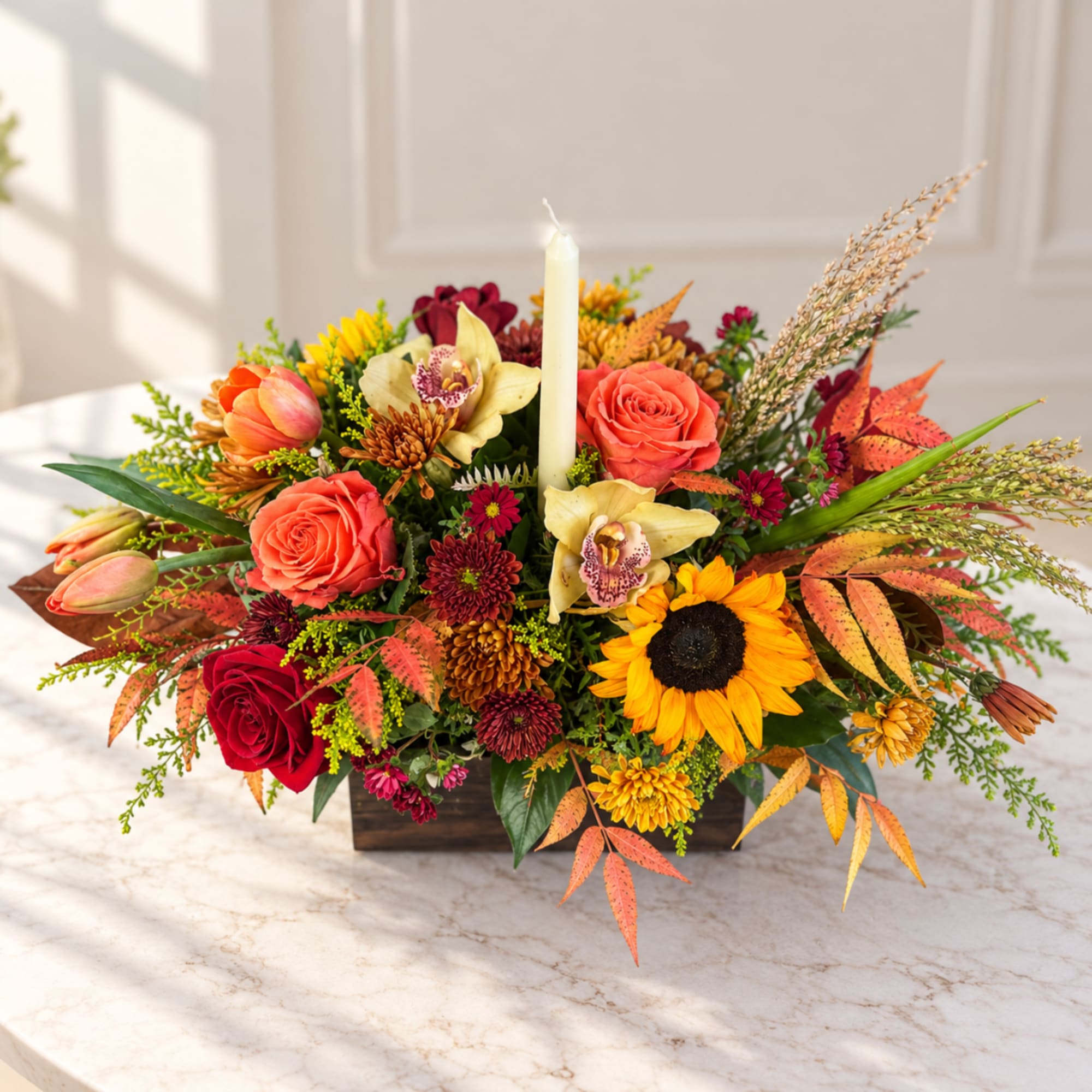 Autumn floral centerpiece with roses, sunflowers, orchids, and a candle in a wooden box