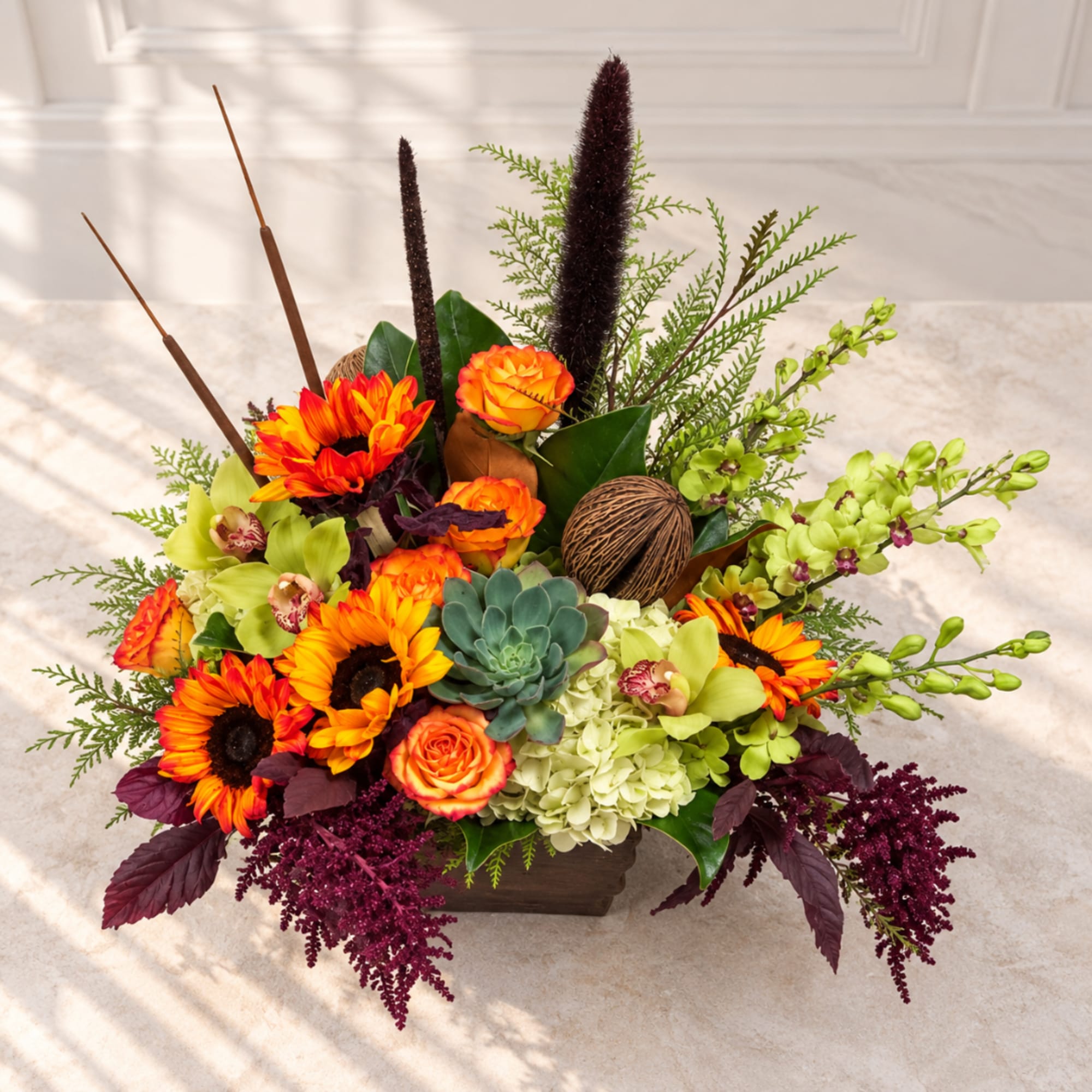 Colorful floral arrangement with sunflowers, roses, orchids, and succulents in a low wooden container