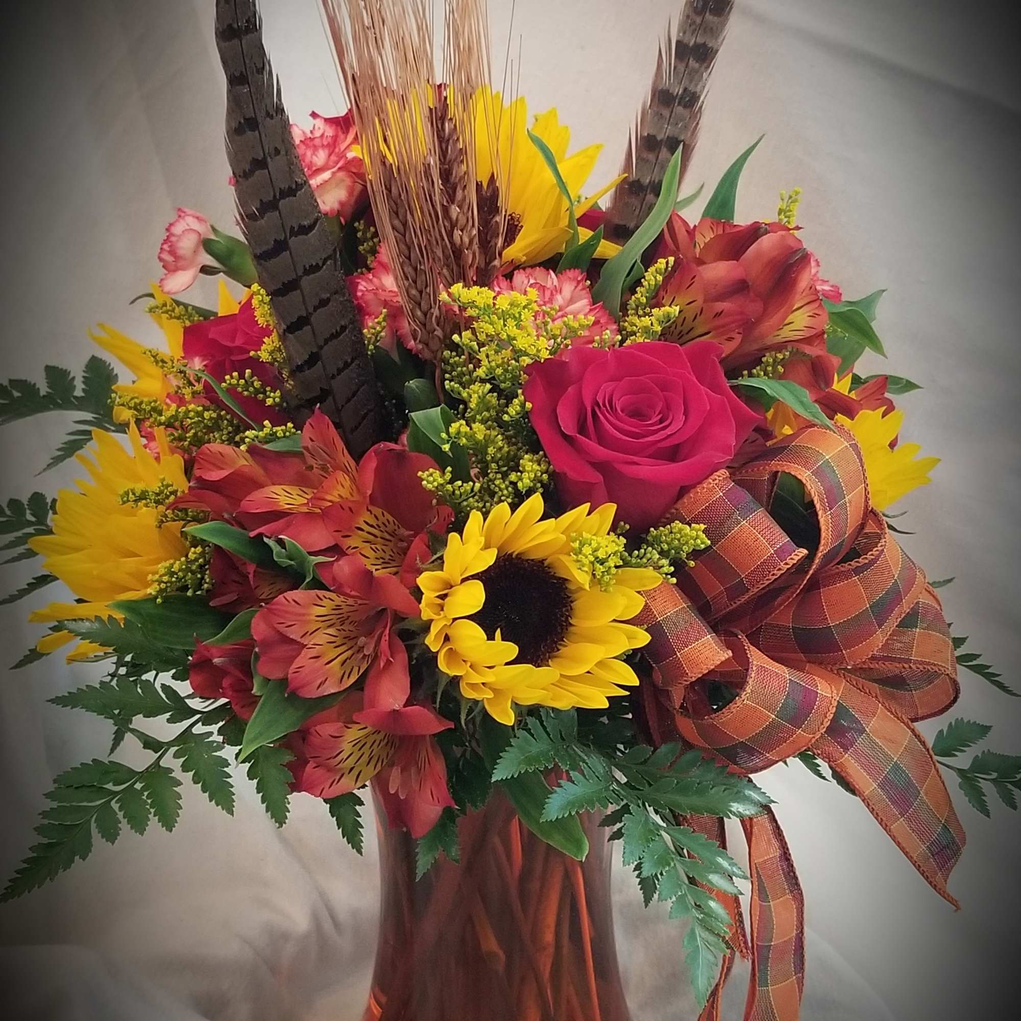 A traditional arrangement of roses, sunflowers asters, alstroemeria and other flowers accented