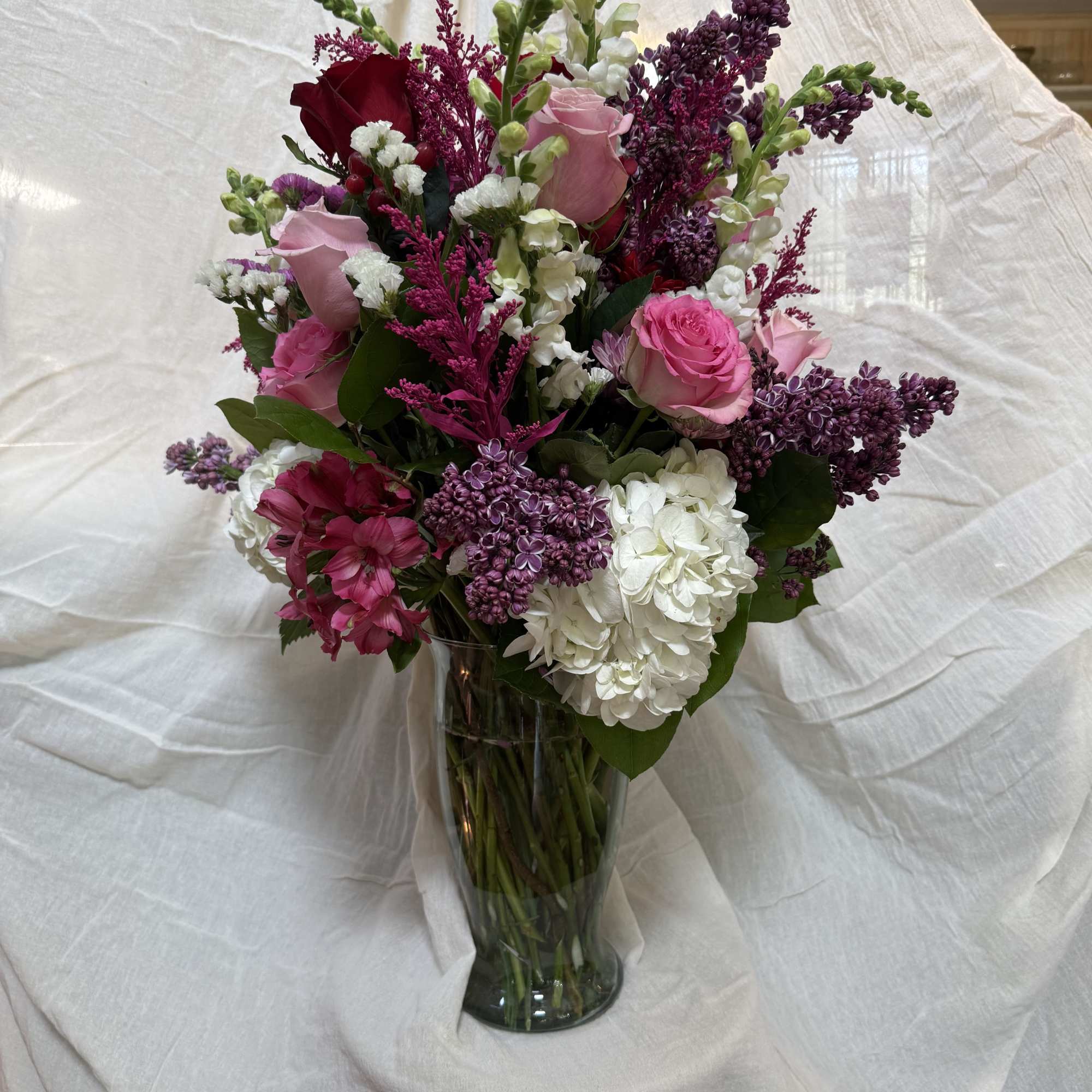 Mixed pink, white, and purple flowers arranged in a clear glass vase.