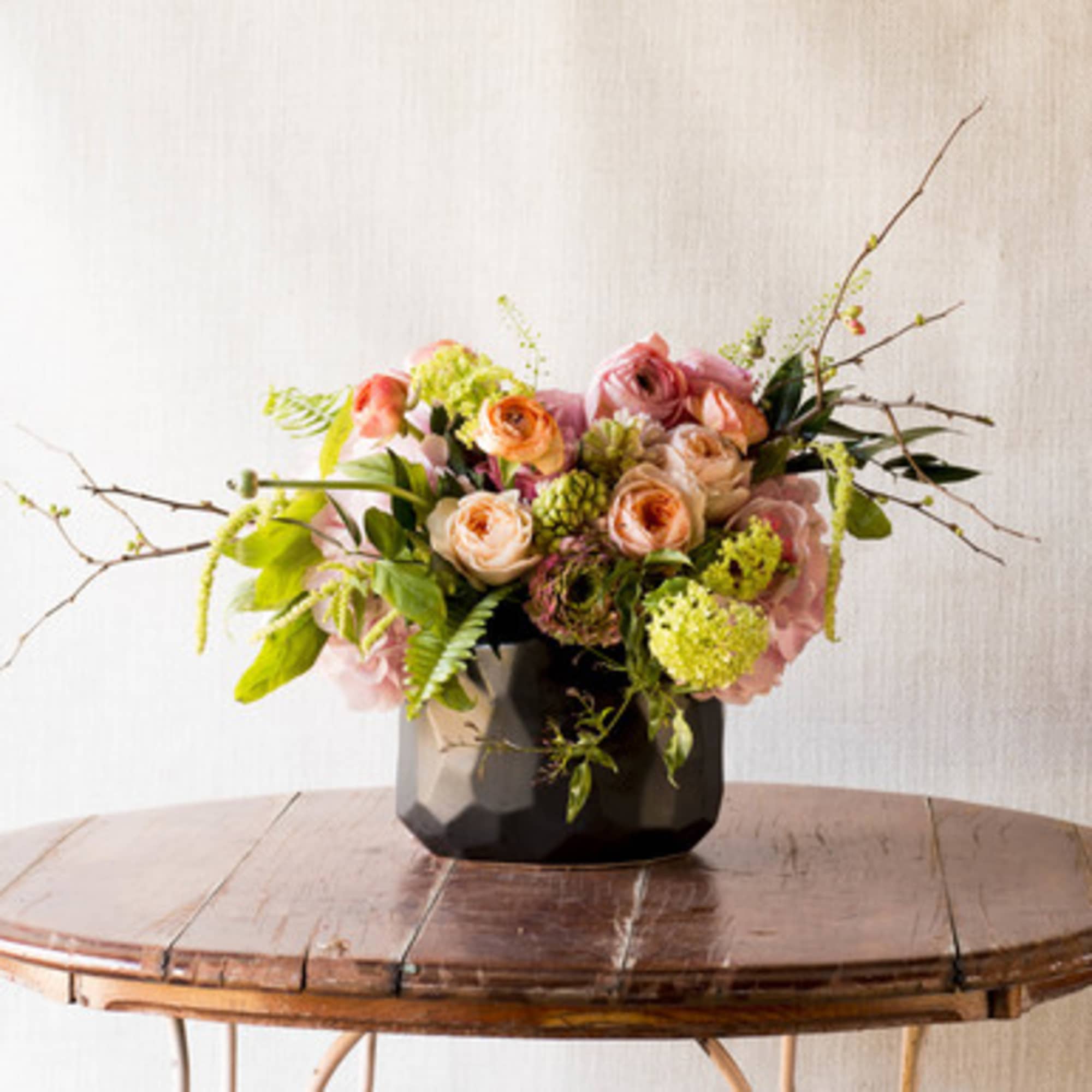Mixed pink and peach flowers in a black vase on a wooden table