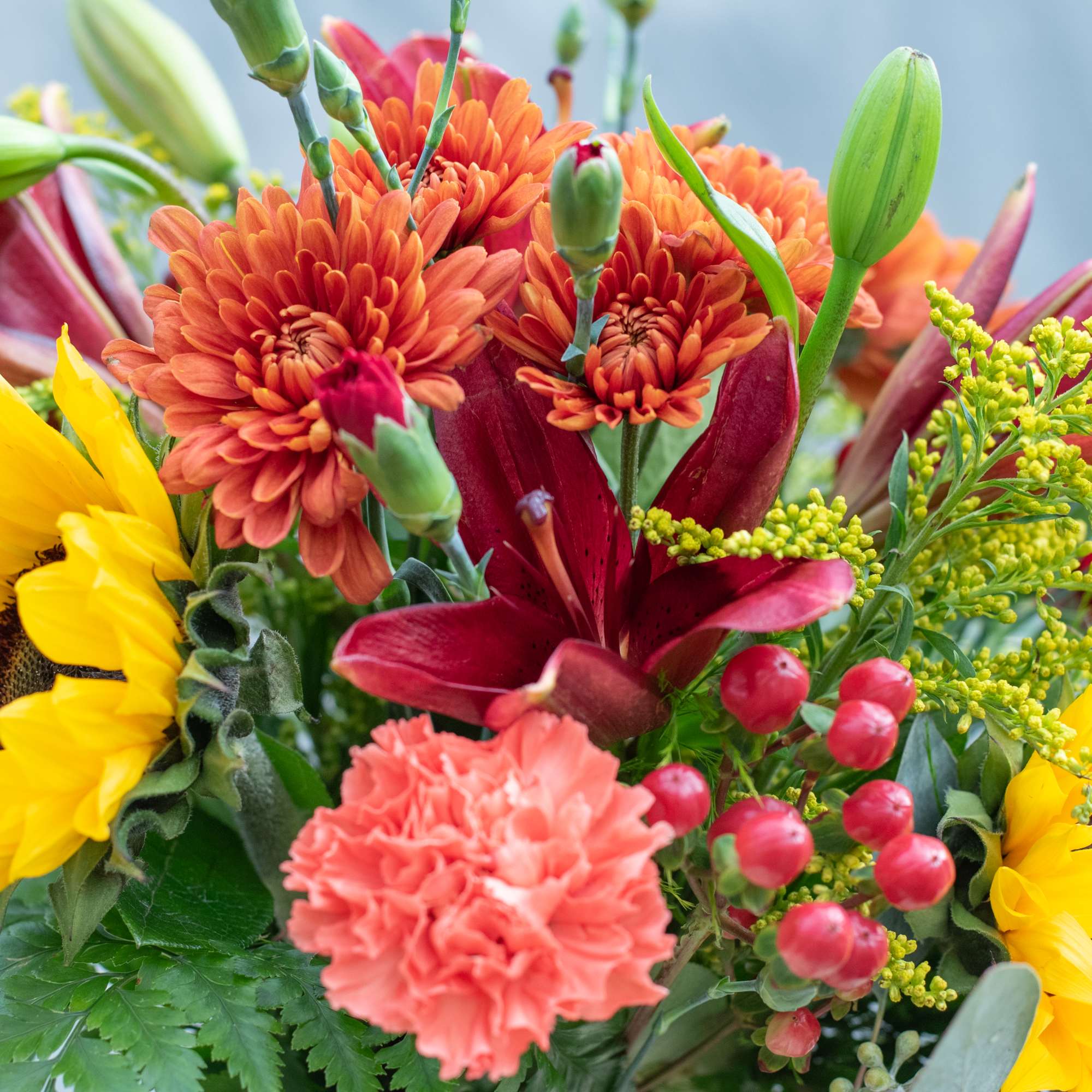 Mixed bouquet with orange mums, red lilies, yellow sunflowers, and pink carnations