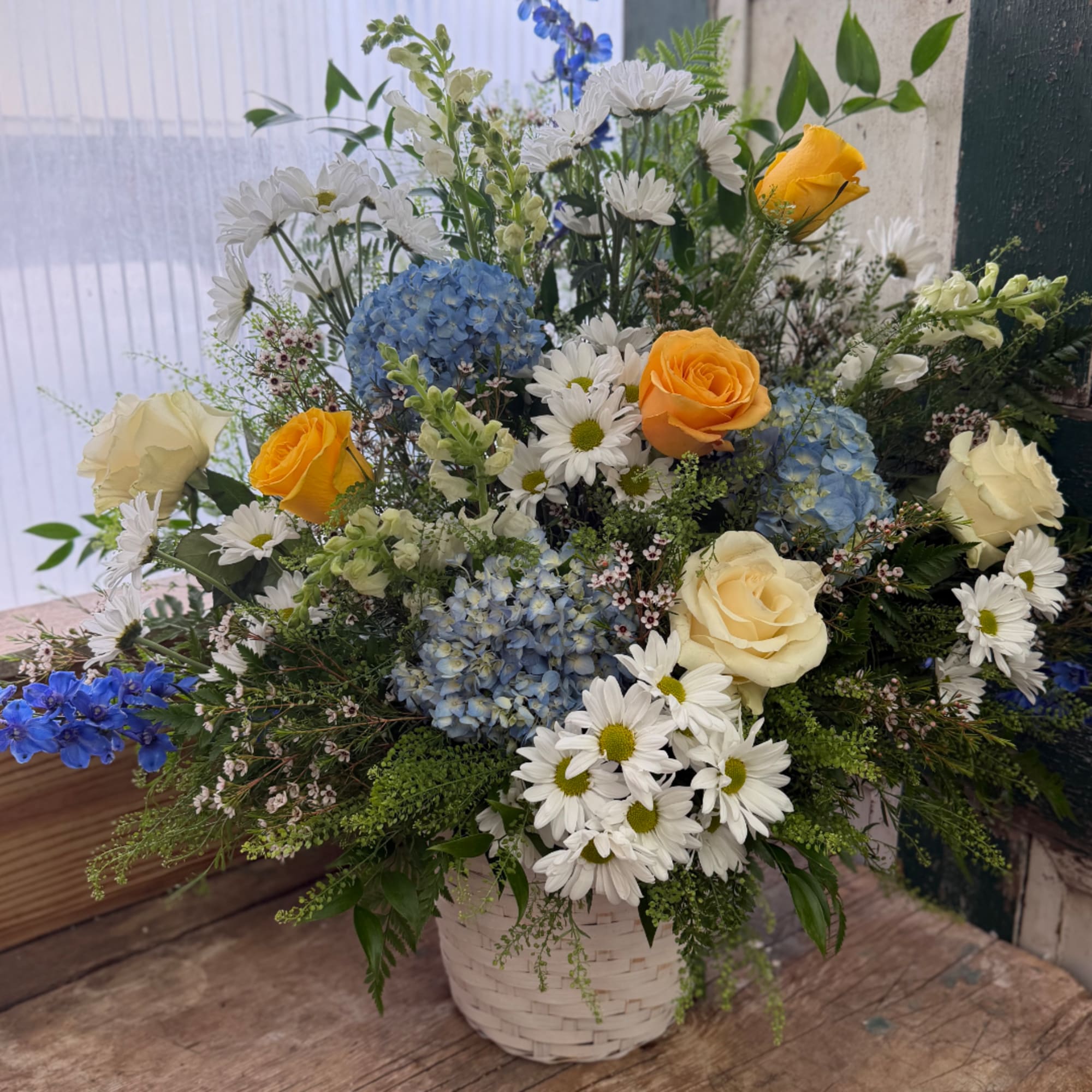Mixed bouquet of roses, daisies, and blue hydrangeas in a white basket