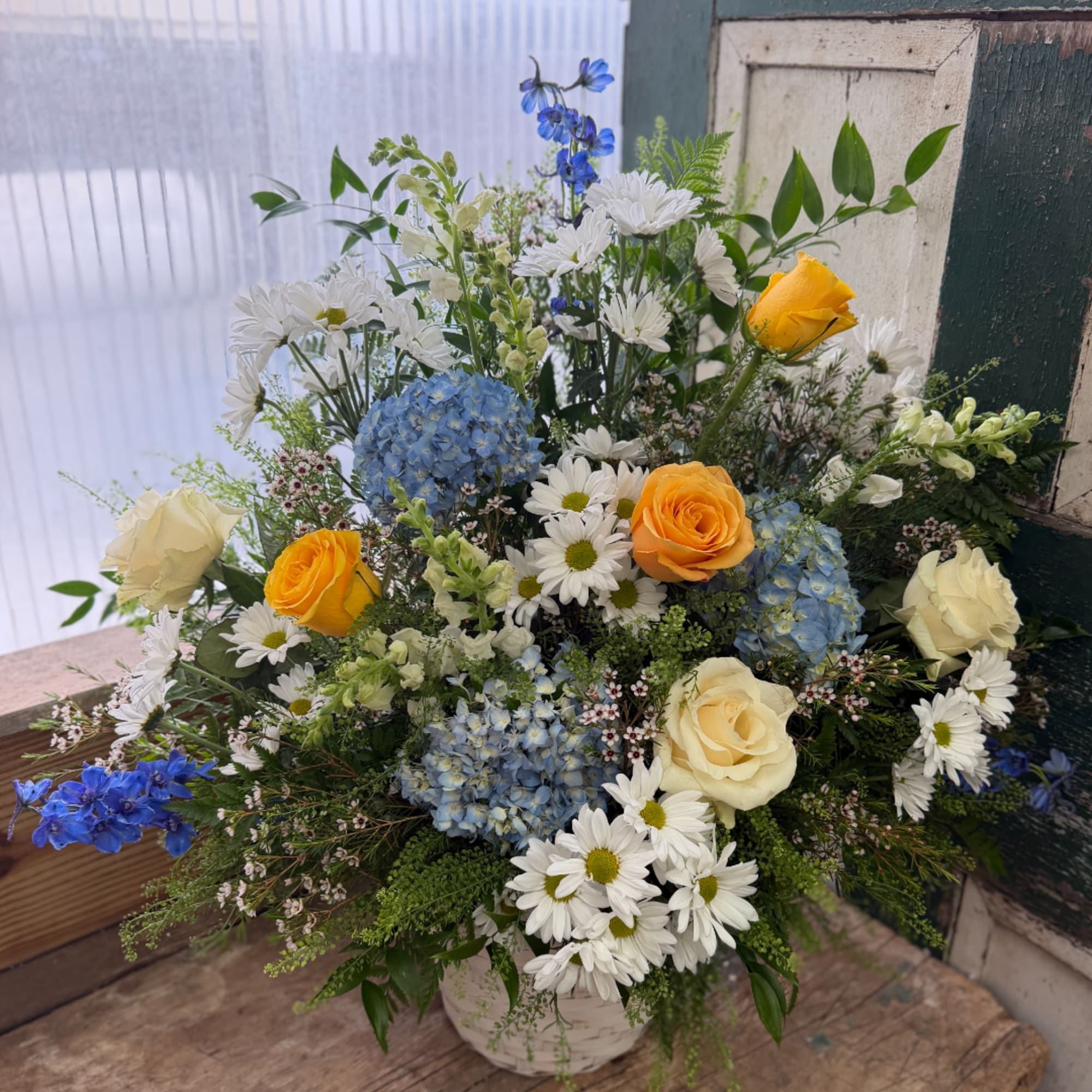 Mixed bouquet of white daisies, blue hydrangeas, and yellow roses in a white container