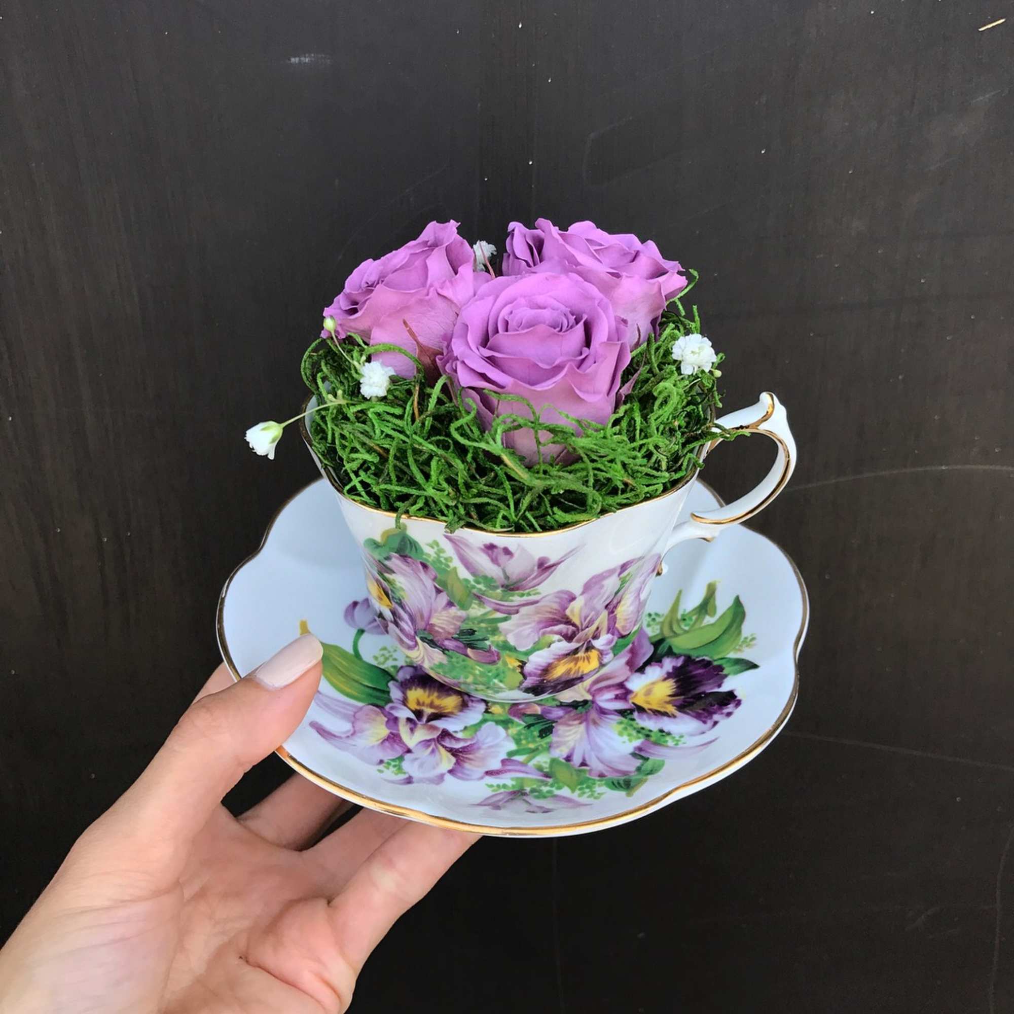 Purple roses arranged in a floral teacup and saucer