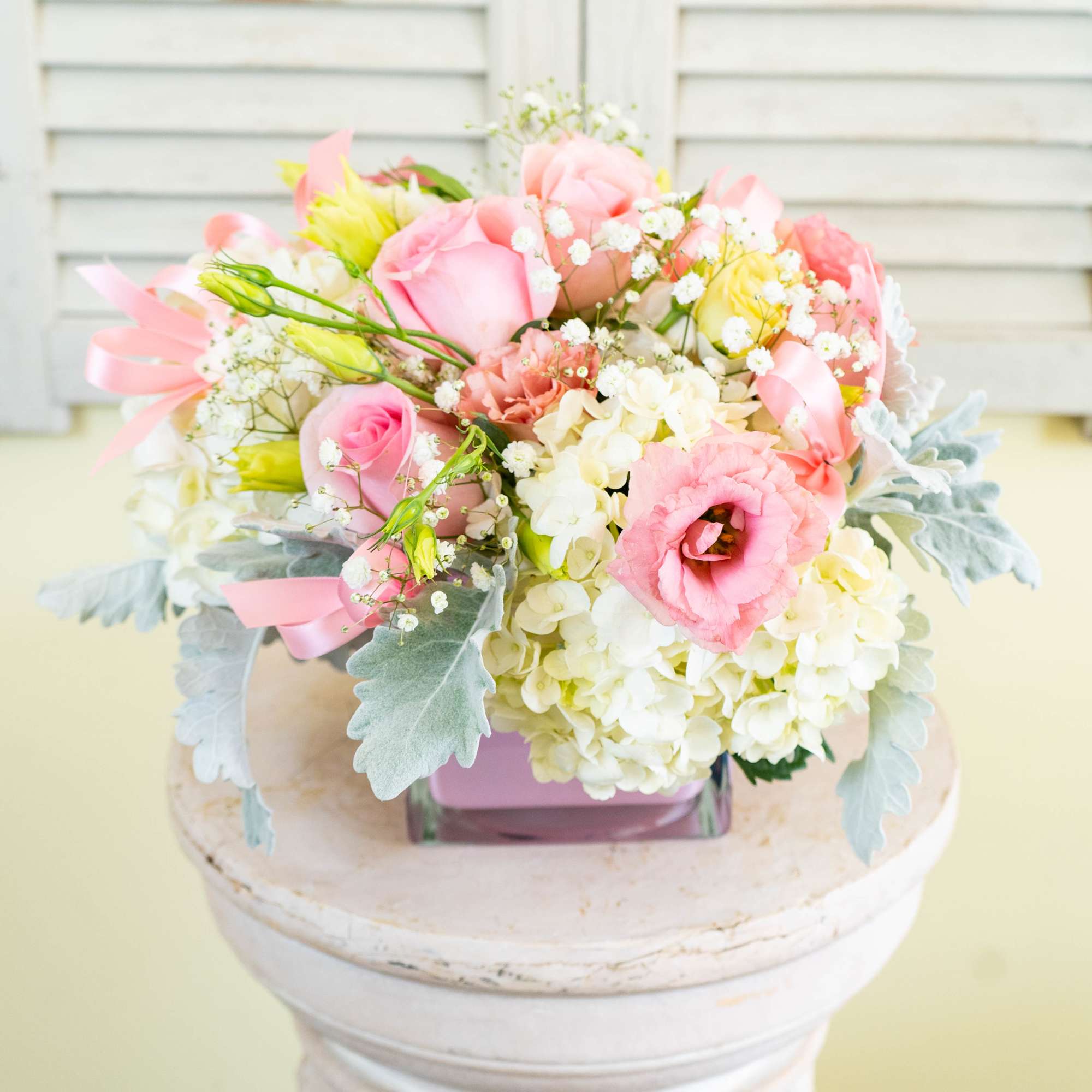 Pink and white bouquet with roses, hydrangeas, and ribbon in a glass vase
