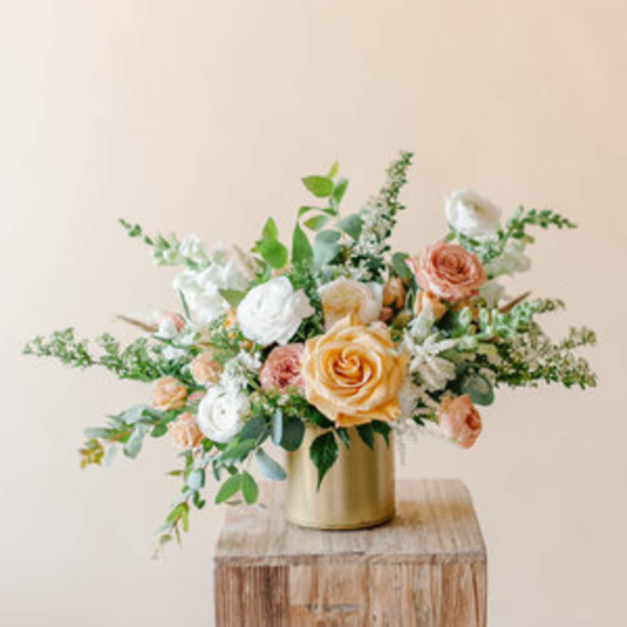 Peach and white roses in a gold vase on a wooden block