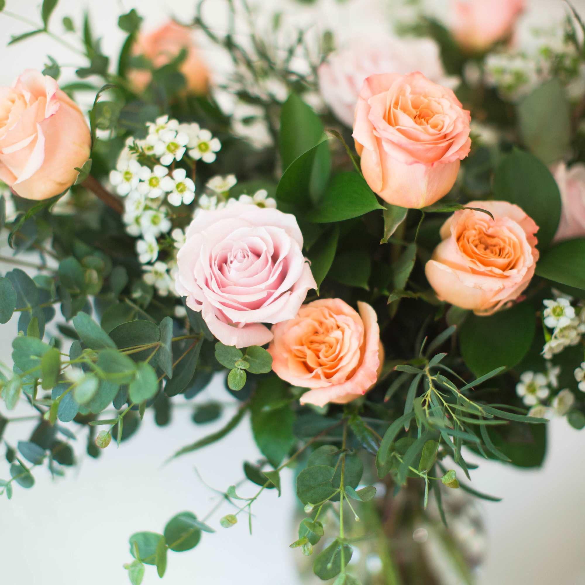 Peach and pale pink roses in a glass vase with greenery
