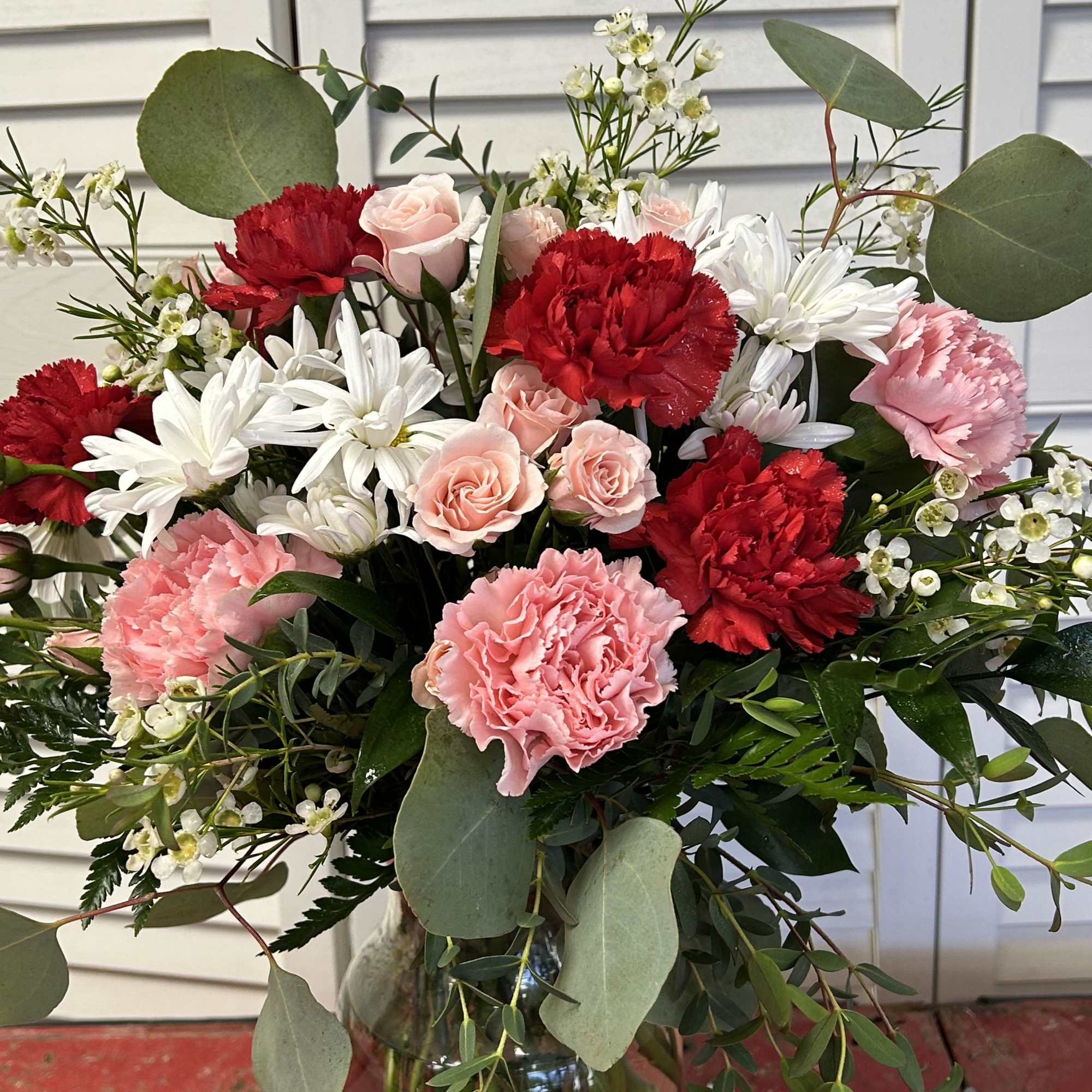 Bouquet of red and pink carnations with white daisies in a glass vase